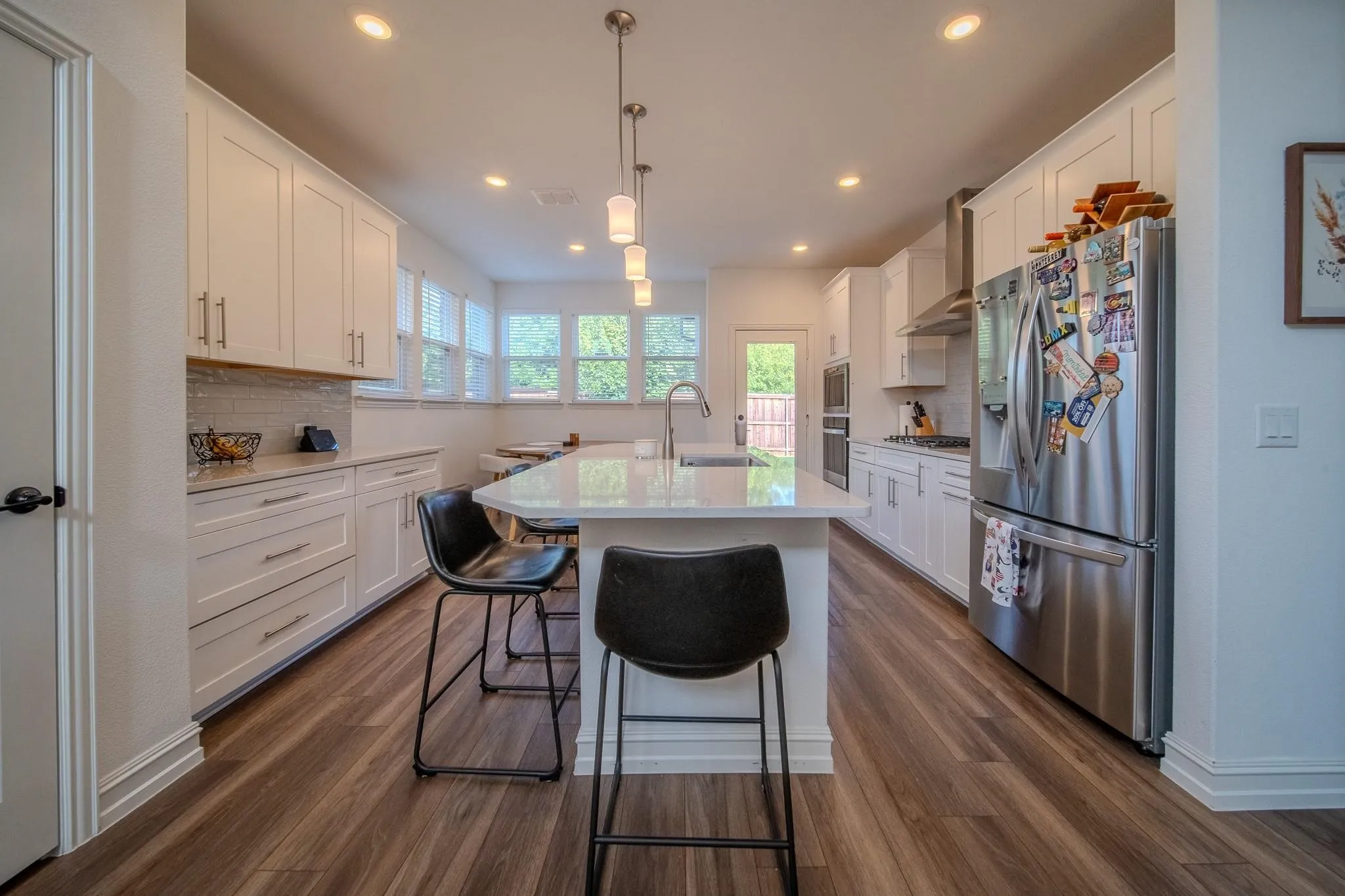 Gourmet kitchen with wood-finish flooring, white cabinetry, a large island with seating, pendant lighting, and stainless steel appliances