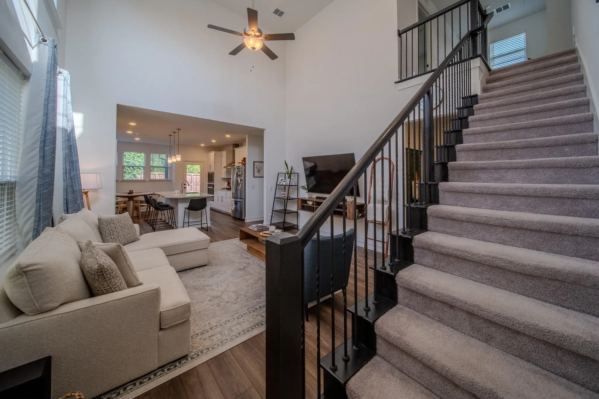 Two-story ceiling, wood-finish flooring, open-concept design, recessed lighting, and a contemporary staircase with metal balusters