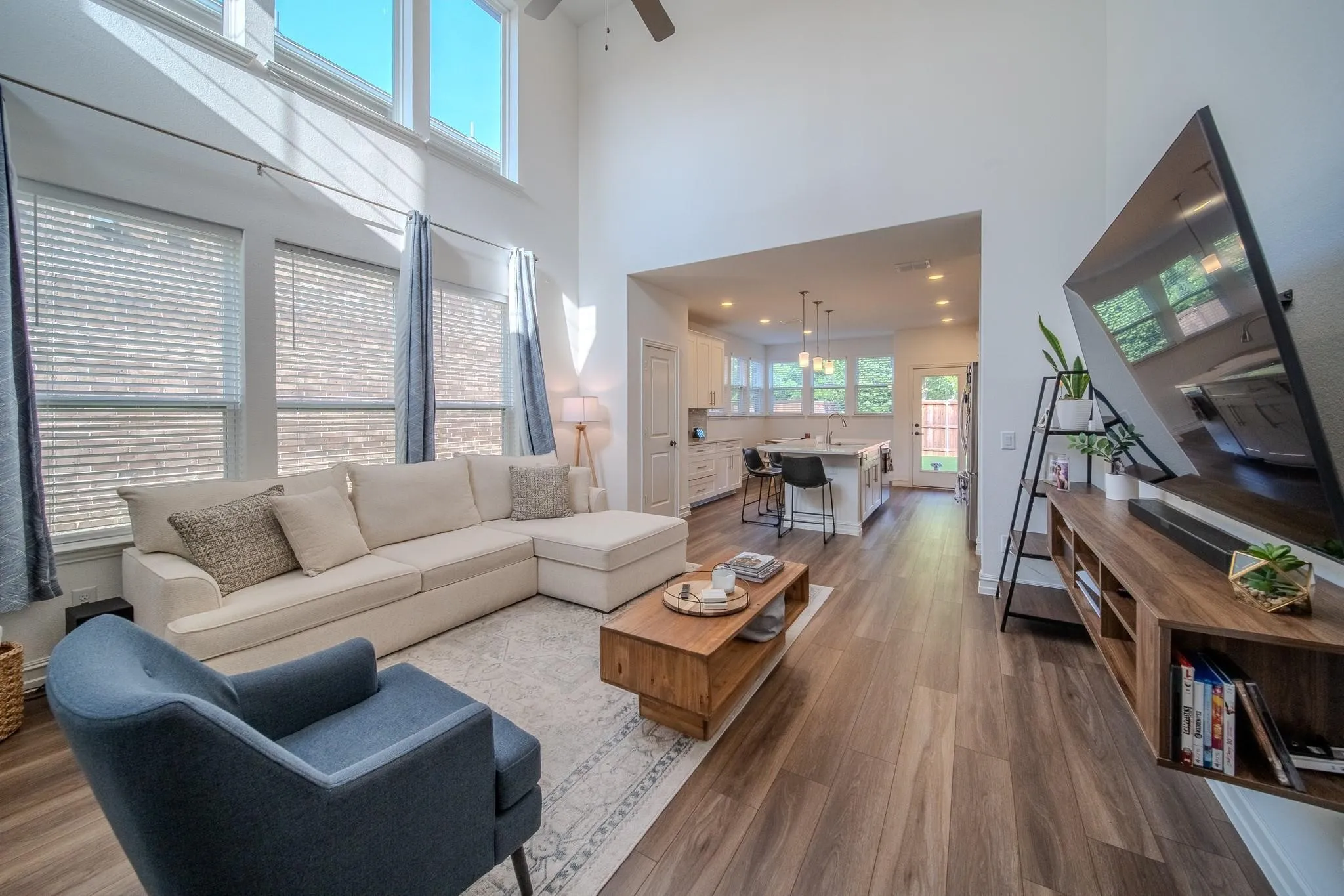 Two-story living area with high ceilings and expansive windows, wood-finish flooring, and a kitchen with an island and pendant lighting