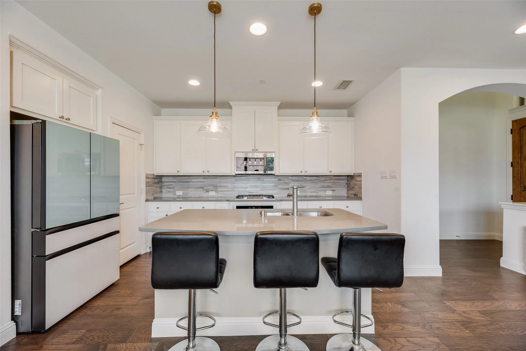 White shaker cabinetry, light-toned countertops, tile backsplash, and dark wood-finish flooring