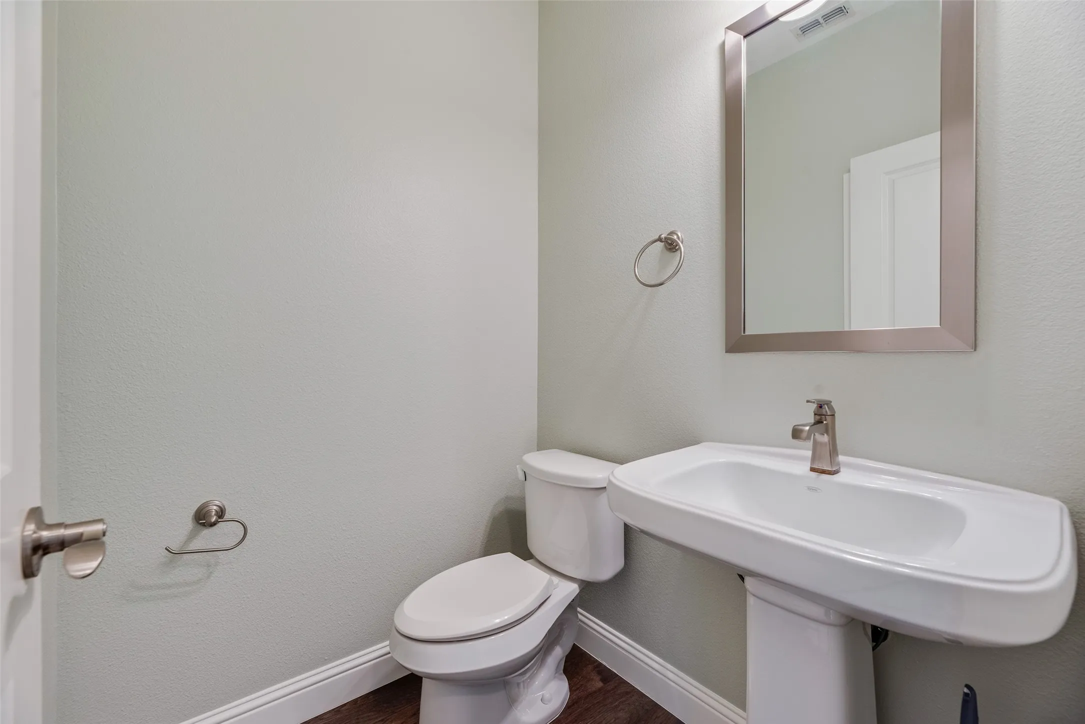 Pedestal sink with a single-handle faucet, rectangular framed mirror, and wood-finish flooring