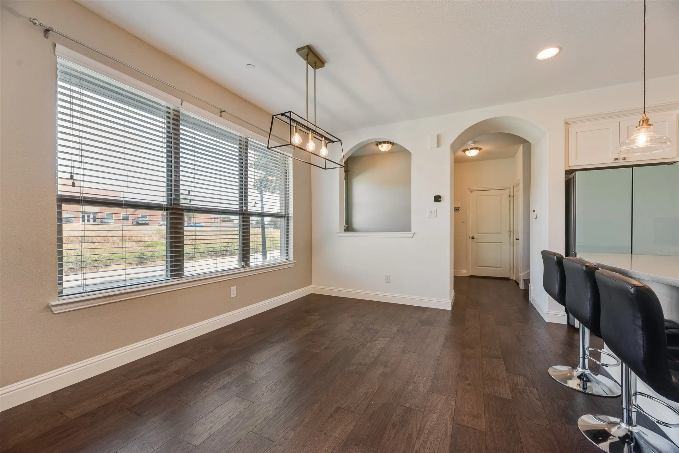 Expansive window with blinds, wood-finish flooring, arched doorways, recessed wall niches, and a modern linear chandelier