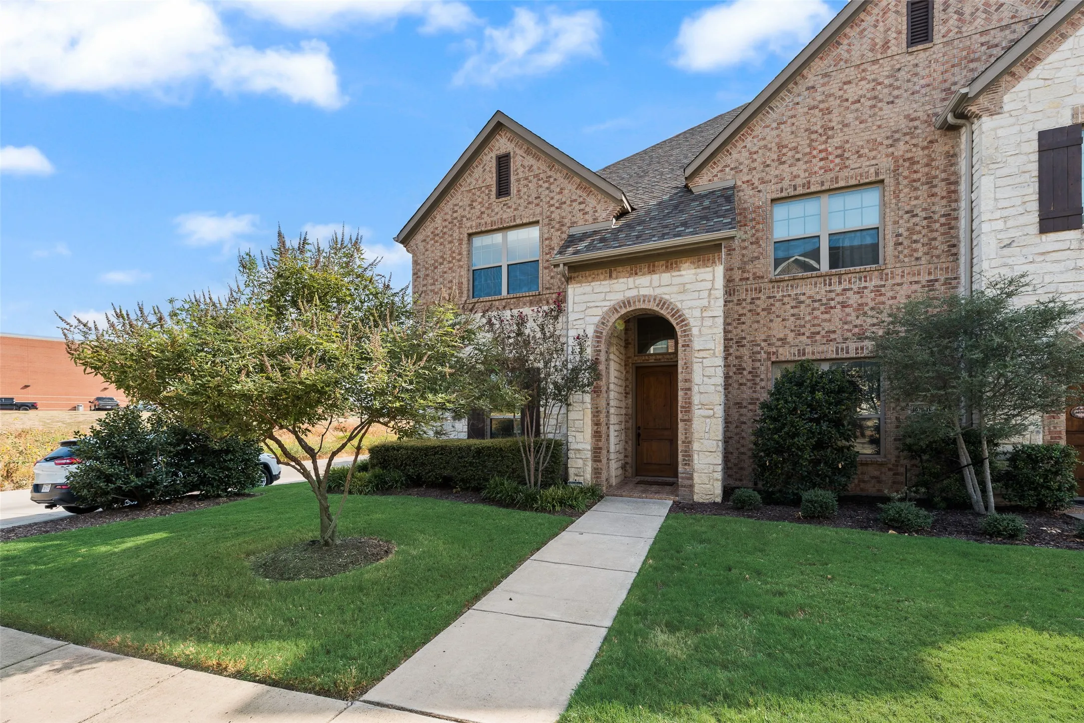 Brick and stone facade featuring an arched entryway, established landscaping, and a concrete walkway