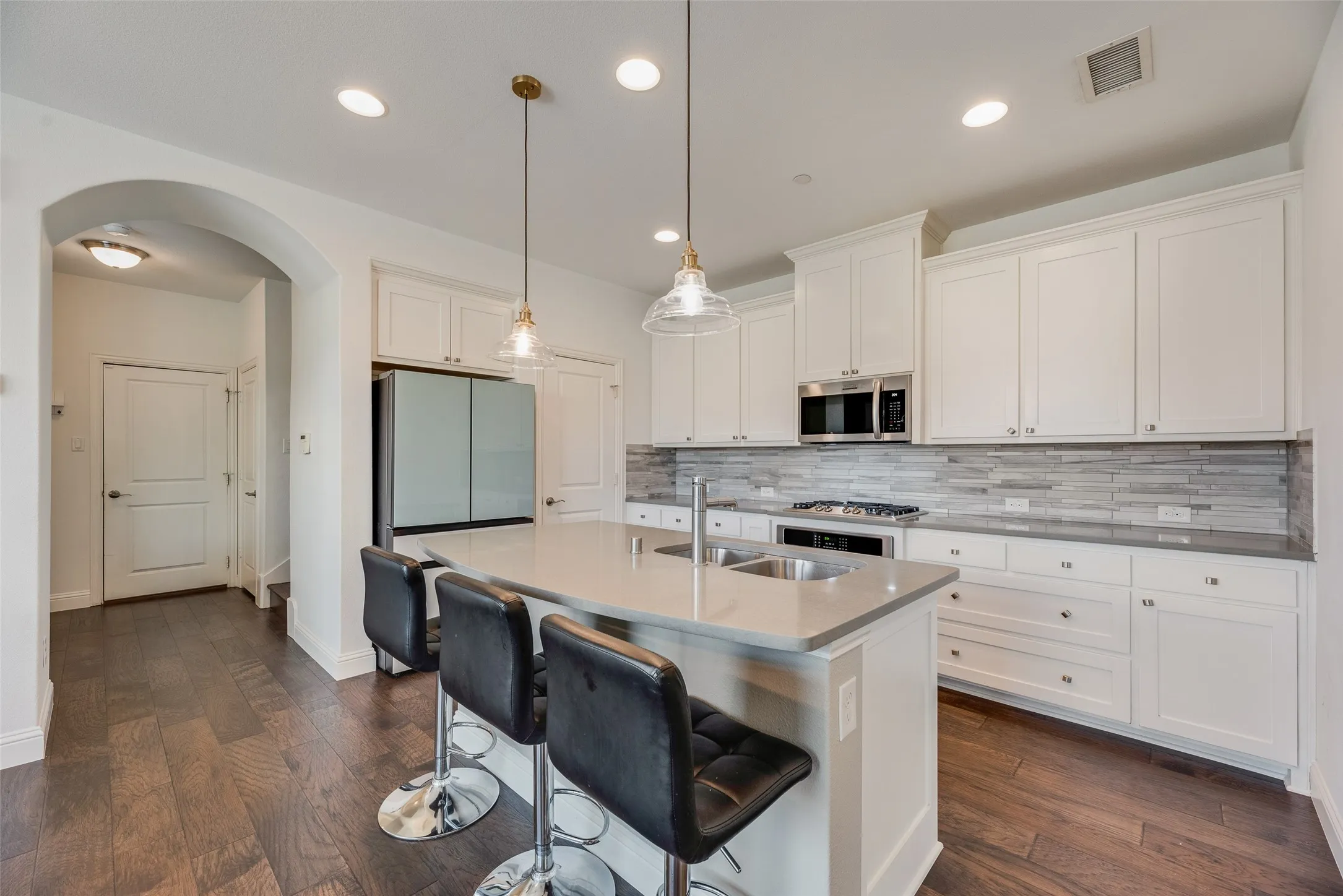 Kitchen featuring white cabinetry, stainless steel appliances, a multi-tone tile backsplash, and a central island with a double basin sink