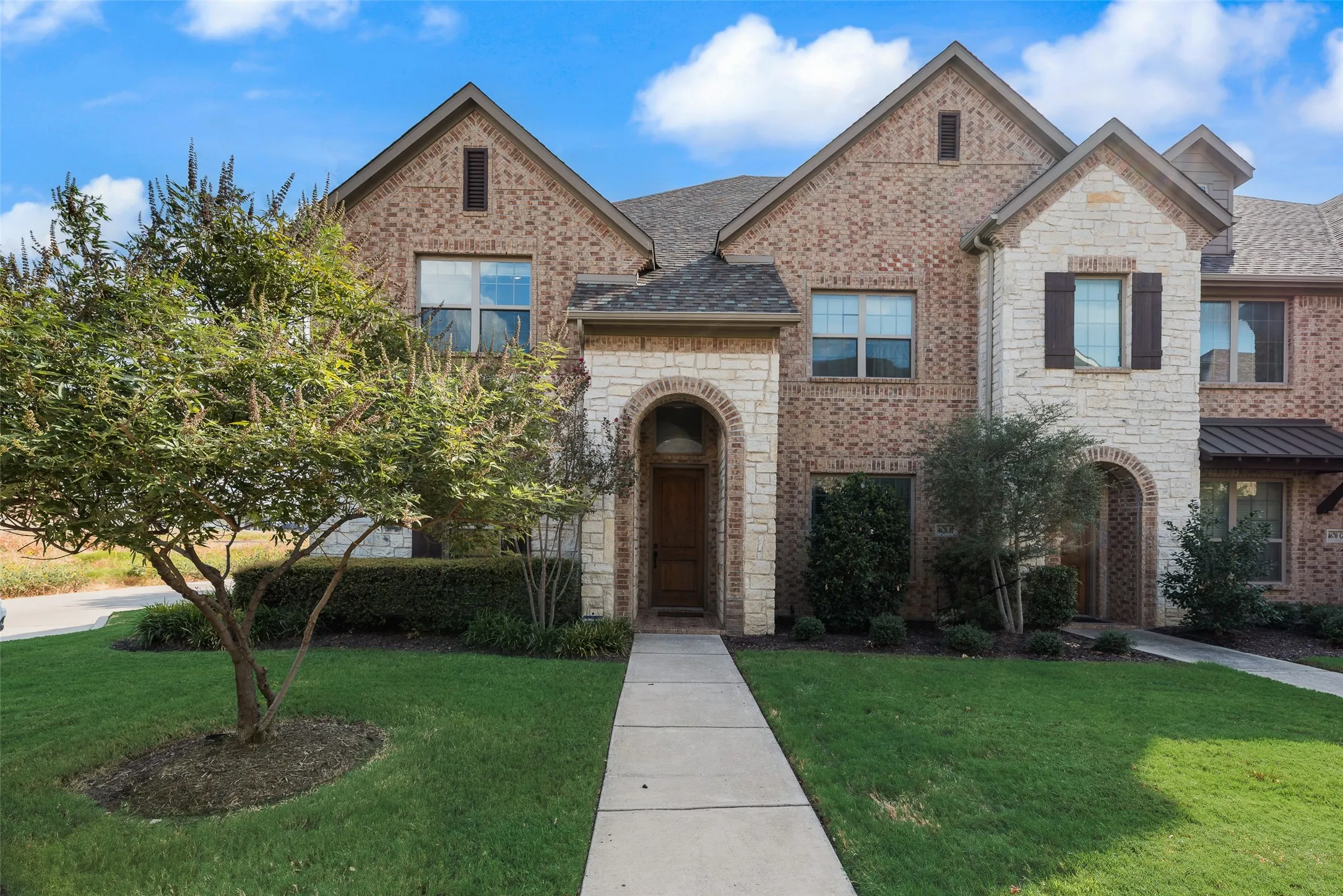 Brick and stone facade featuring arched entryways, gabled rooflines, and mature landscaping