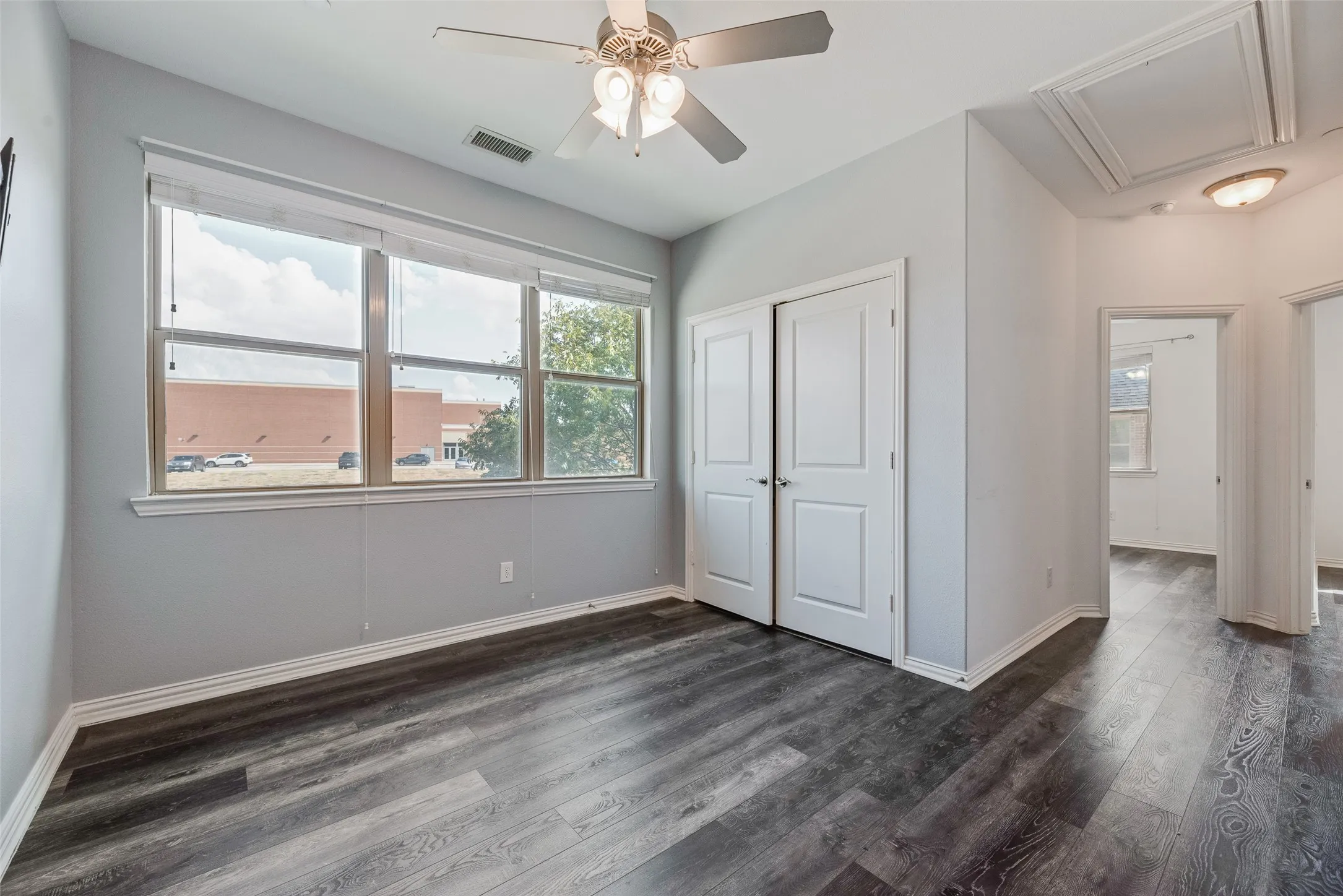 Wood-finish flooring throughout, ceiling fan with integrated lighting, multiple windows providing natural light, white paneled doors, and access panel