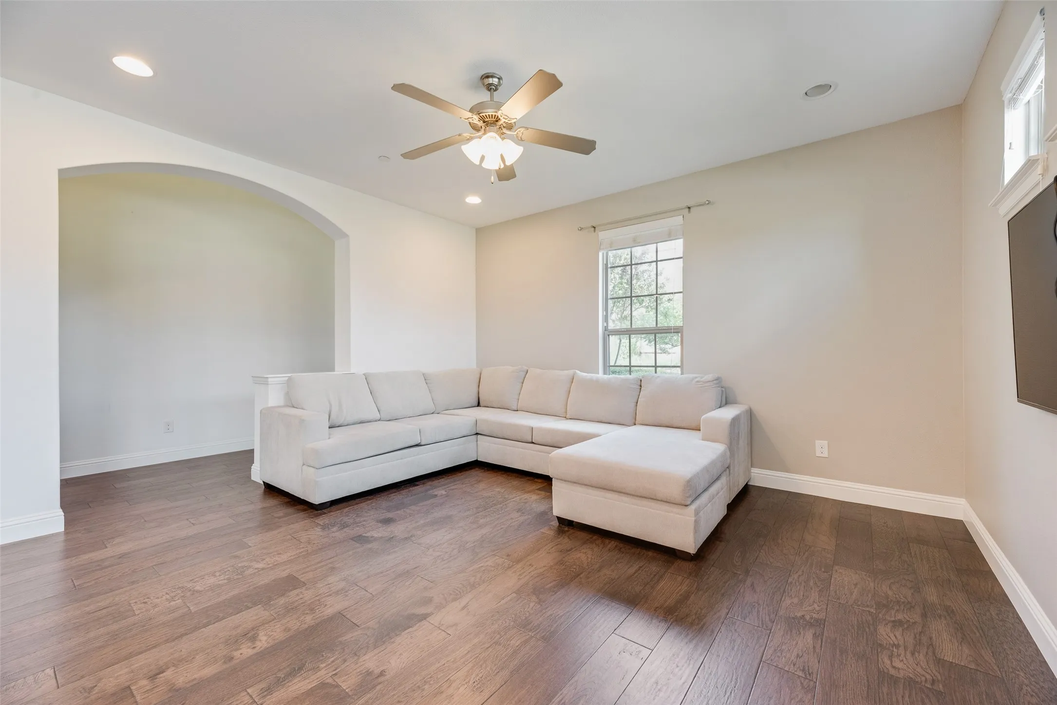 Wood-finish flooring, recessed lighting, ceiling fan with integrated light, arched doorway, and window with white trim