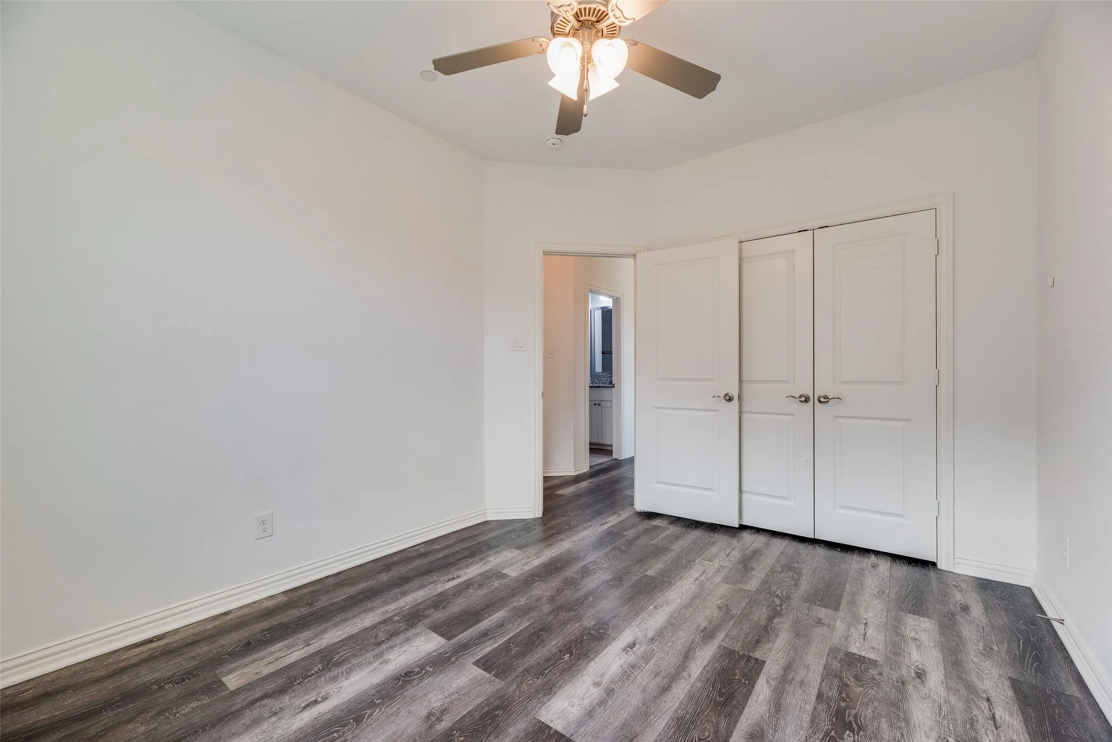 Wood-finish flooring, white walls, and a ceiling fan with integrated lighting