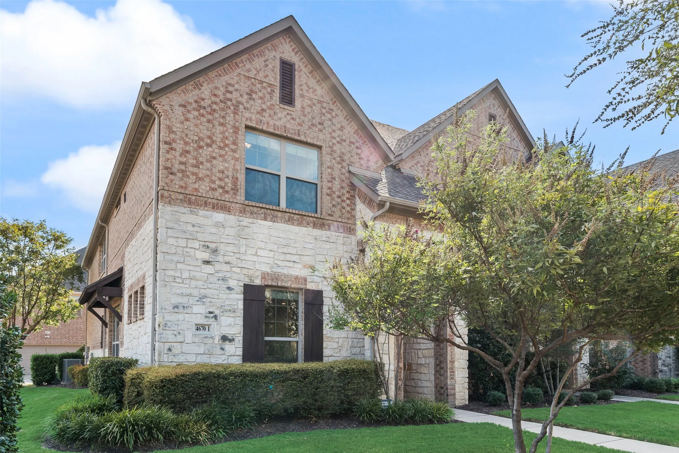 Brick and stone exterior featuring gabled rooflines, dark window shutters, and a covered entry