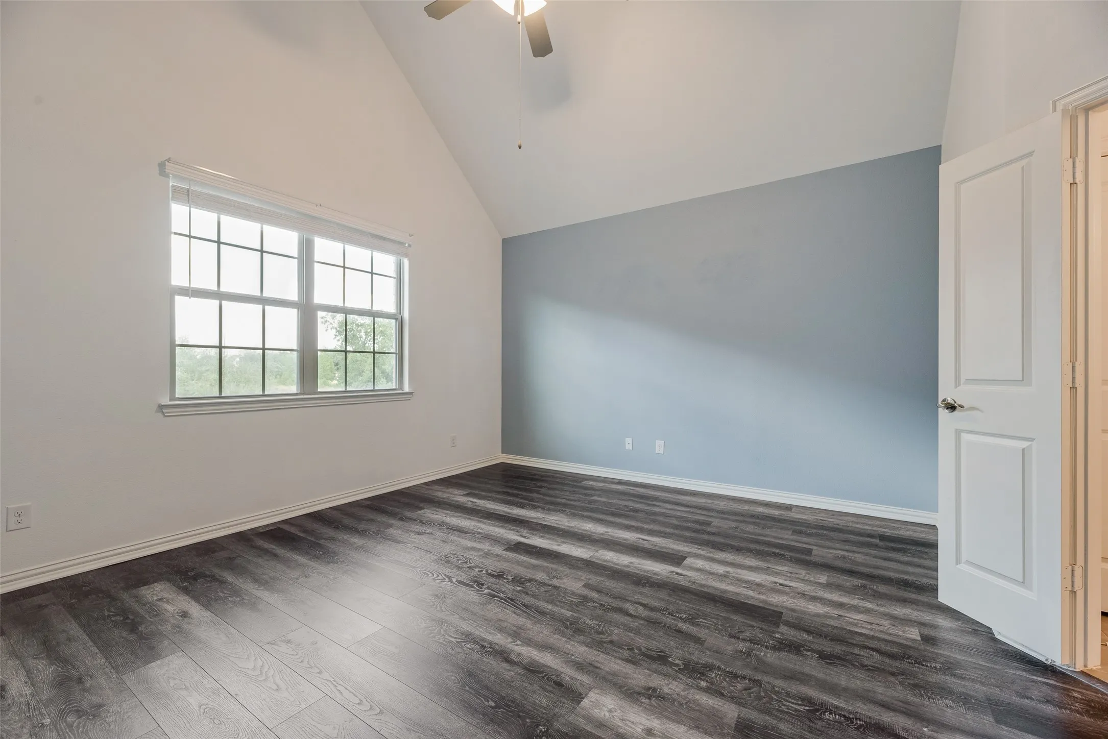 Vaulted ceiling featuring a ceiling fan, wood-finish flooring, and a window with blinds