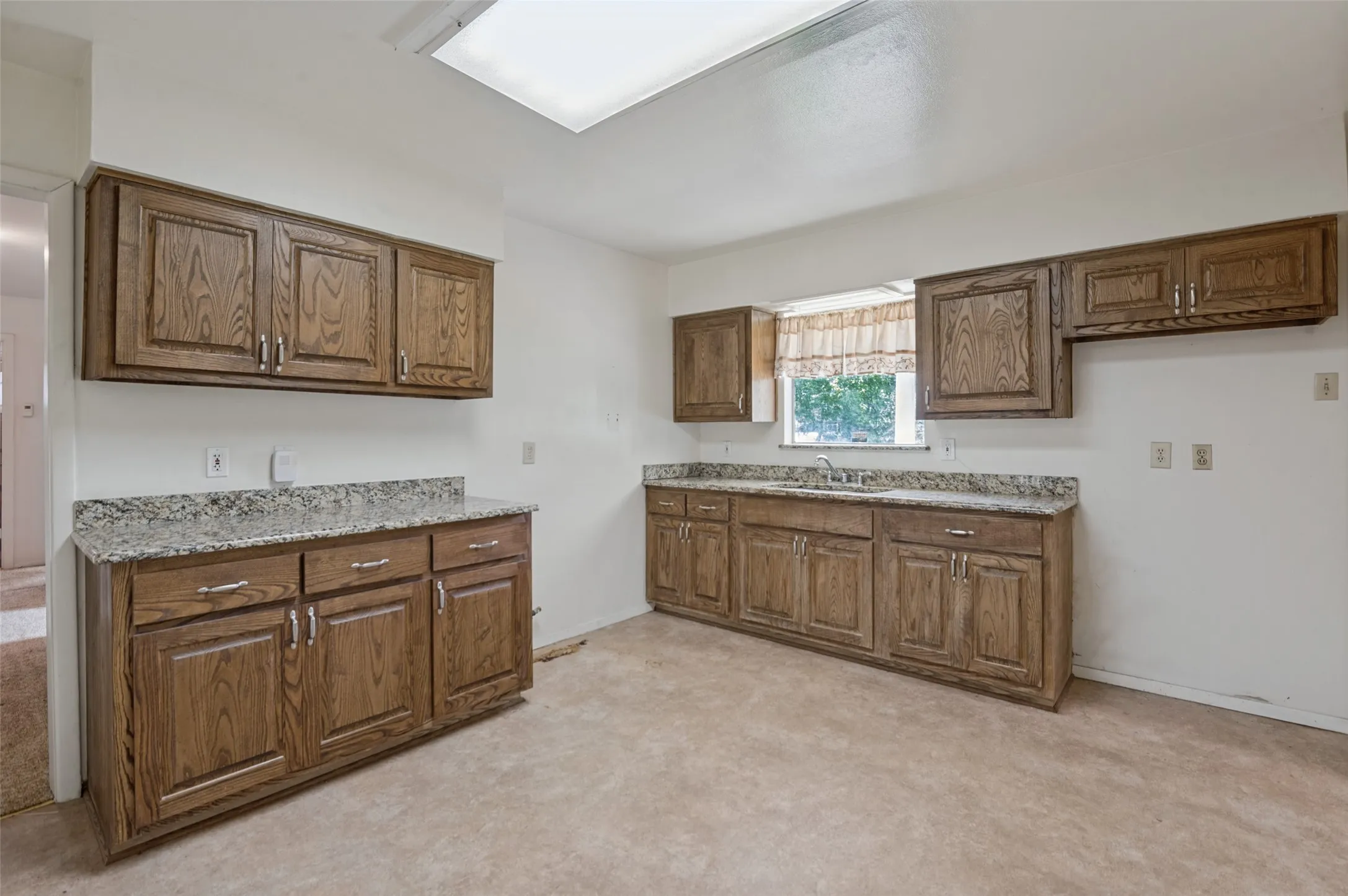 Kitchen with wood-finish cabinetry, light-toned countertops, and a skylight