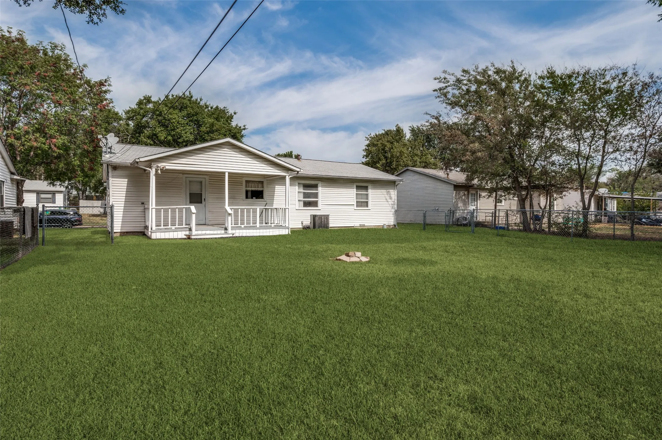 Expansive lawn with a chain-link fence, mature trees, and a covered porch with white railings