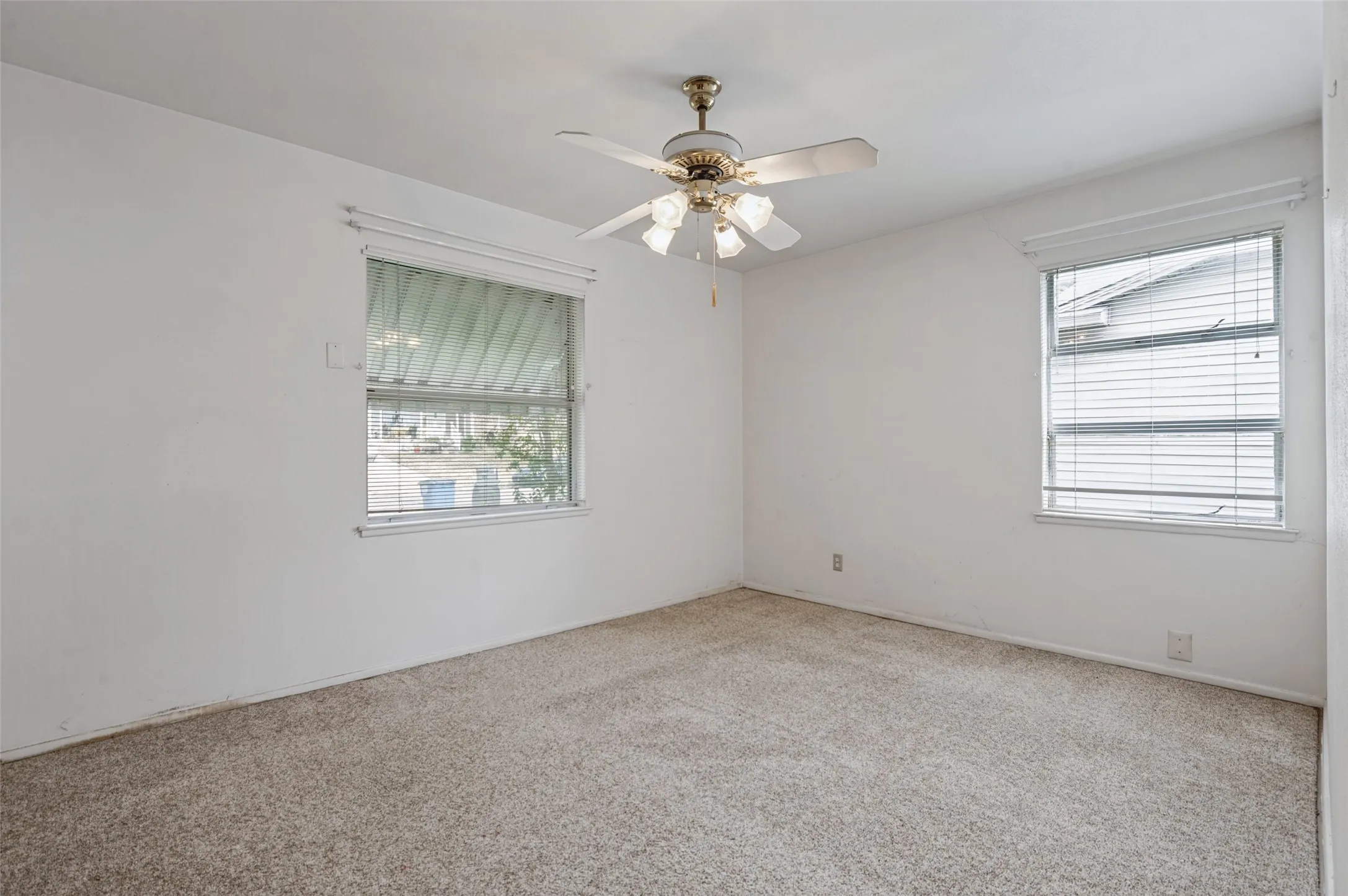 Neutral-toned wall paint, two windows with blinds, and a ceiling fan with integrated lighting