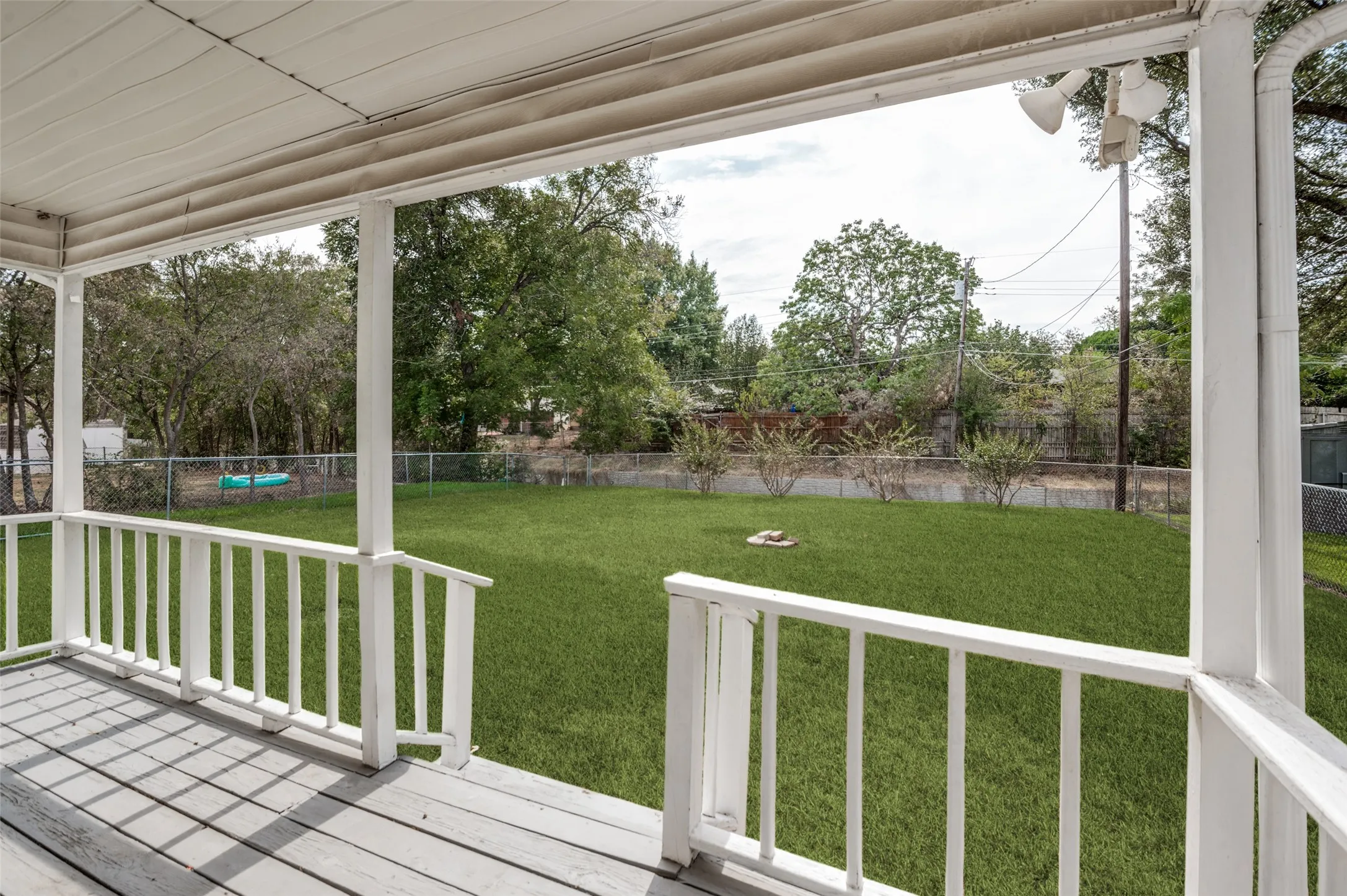 Covered porch with painted wood decking, white railings, and a spacious green lawn