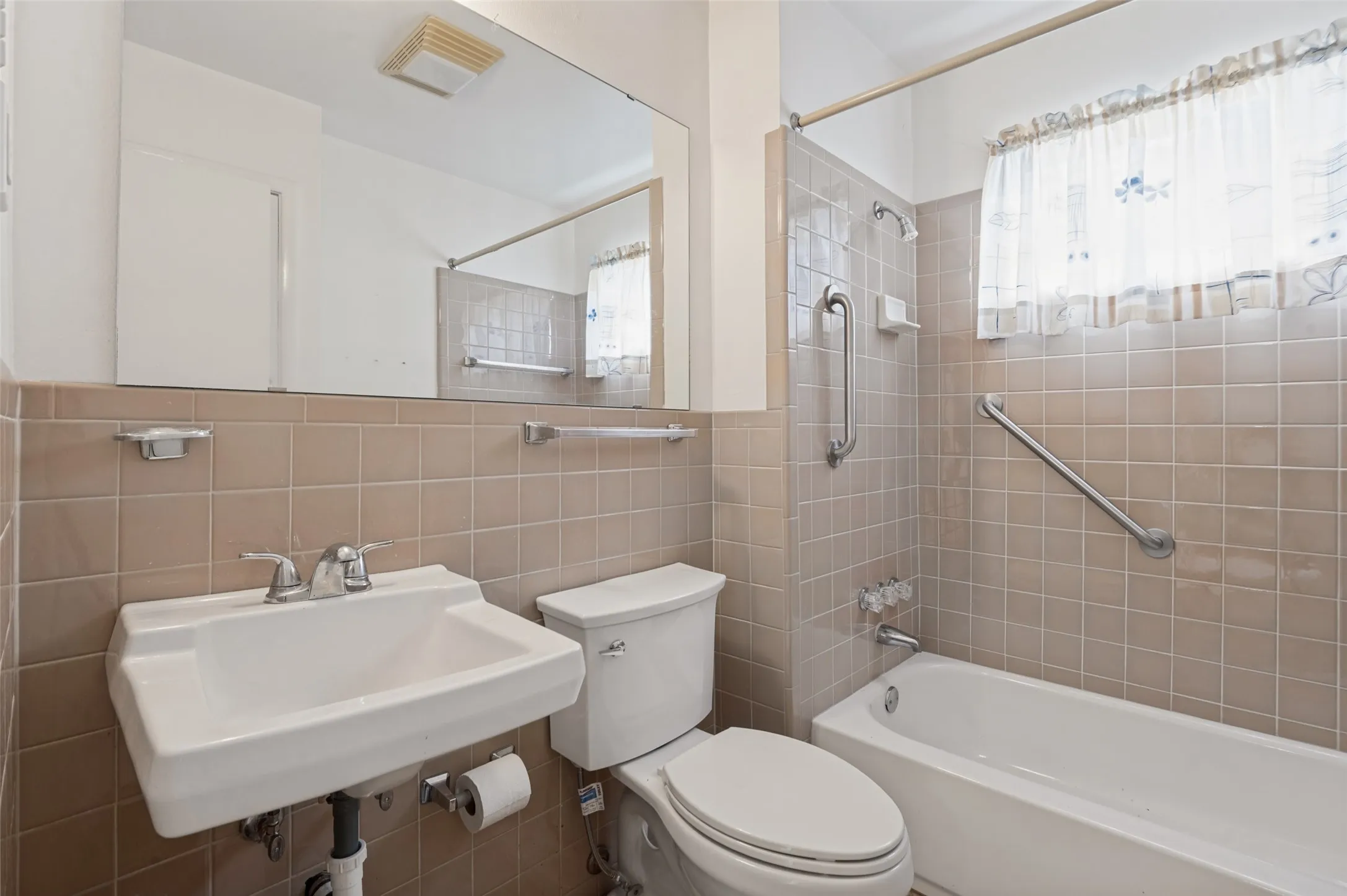 Floor-mounted toilet, wall-mounted sink with chrome faucet, built-in bathtub with chrome fixtures, and wall-mounted grab bars