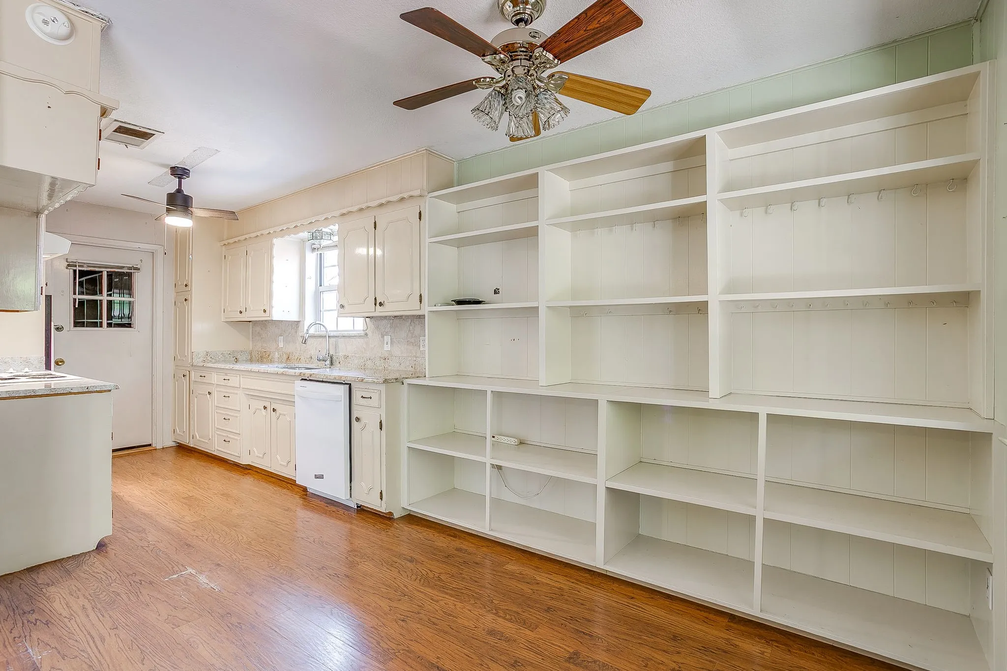 Wood-finish flooring throughout, extensive built-in shelving, white cabinetry, integrated dishwasher, and a ceiling fan