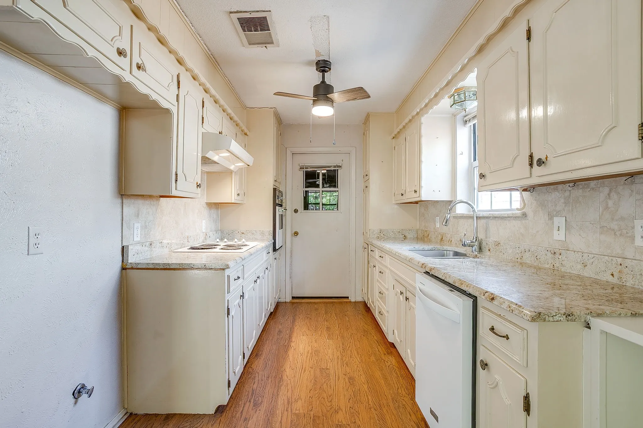 Galley kitchen featuring wood-finish flooring, white cabinetry, integrated appliances, and light-toned countertops