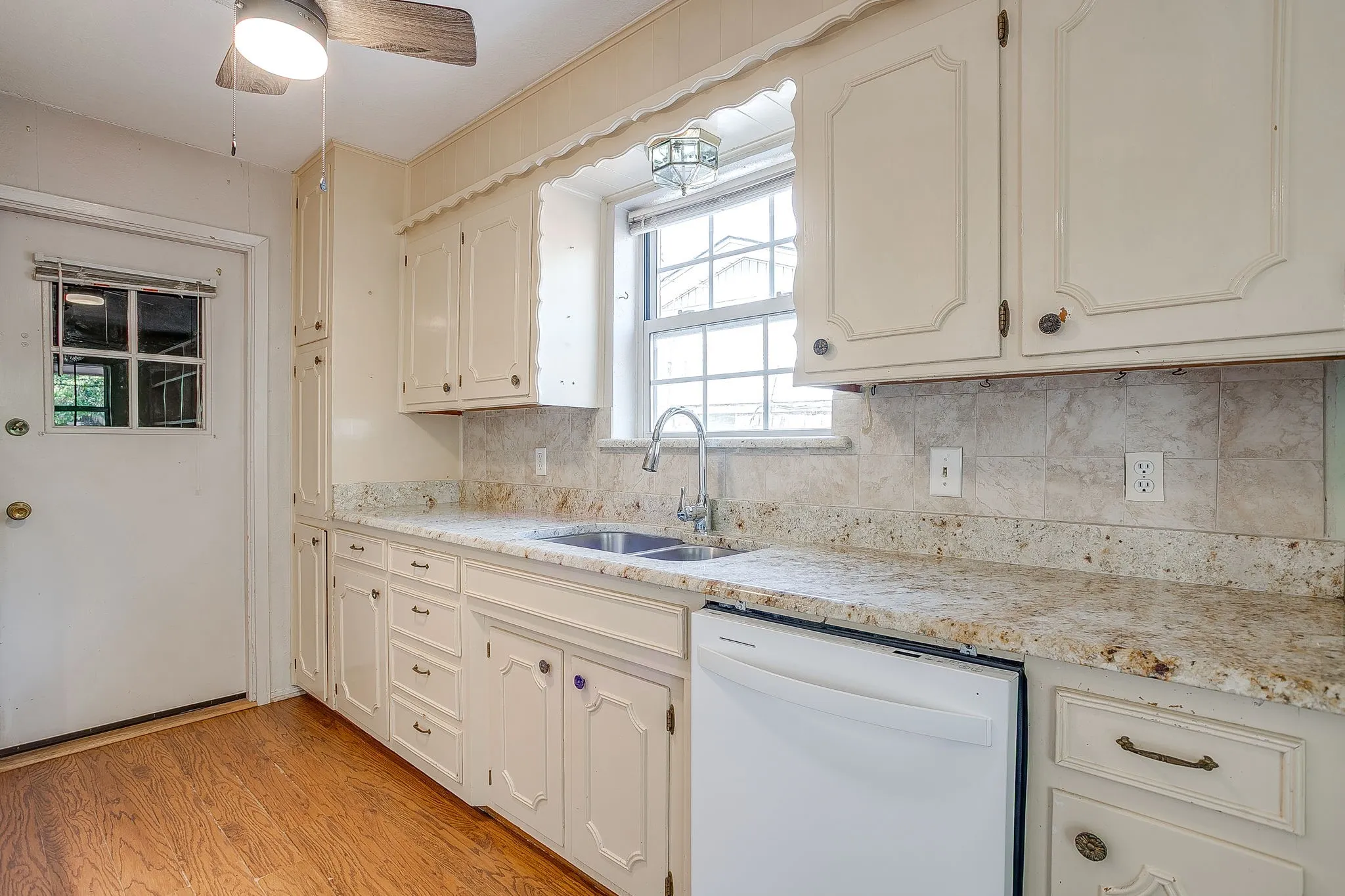 Kitchen featuring light-toned cabinetry, a double basin sink, light-toned countertops, tile backsplash, and wood-finish flooring