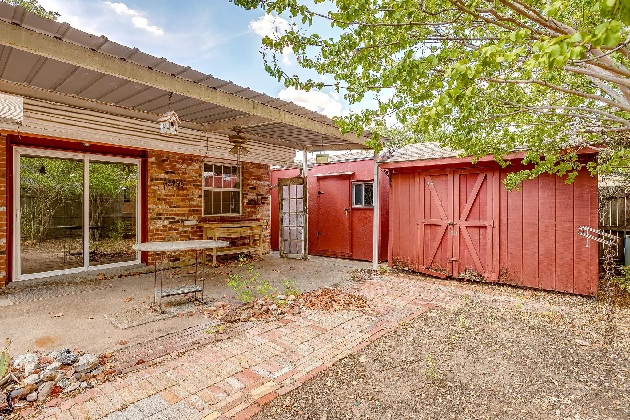 Brick exterior with a covered patio, sliding glass door, and two red storage sheds