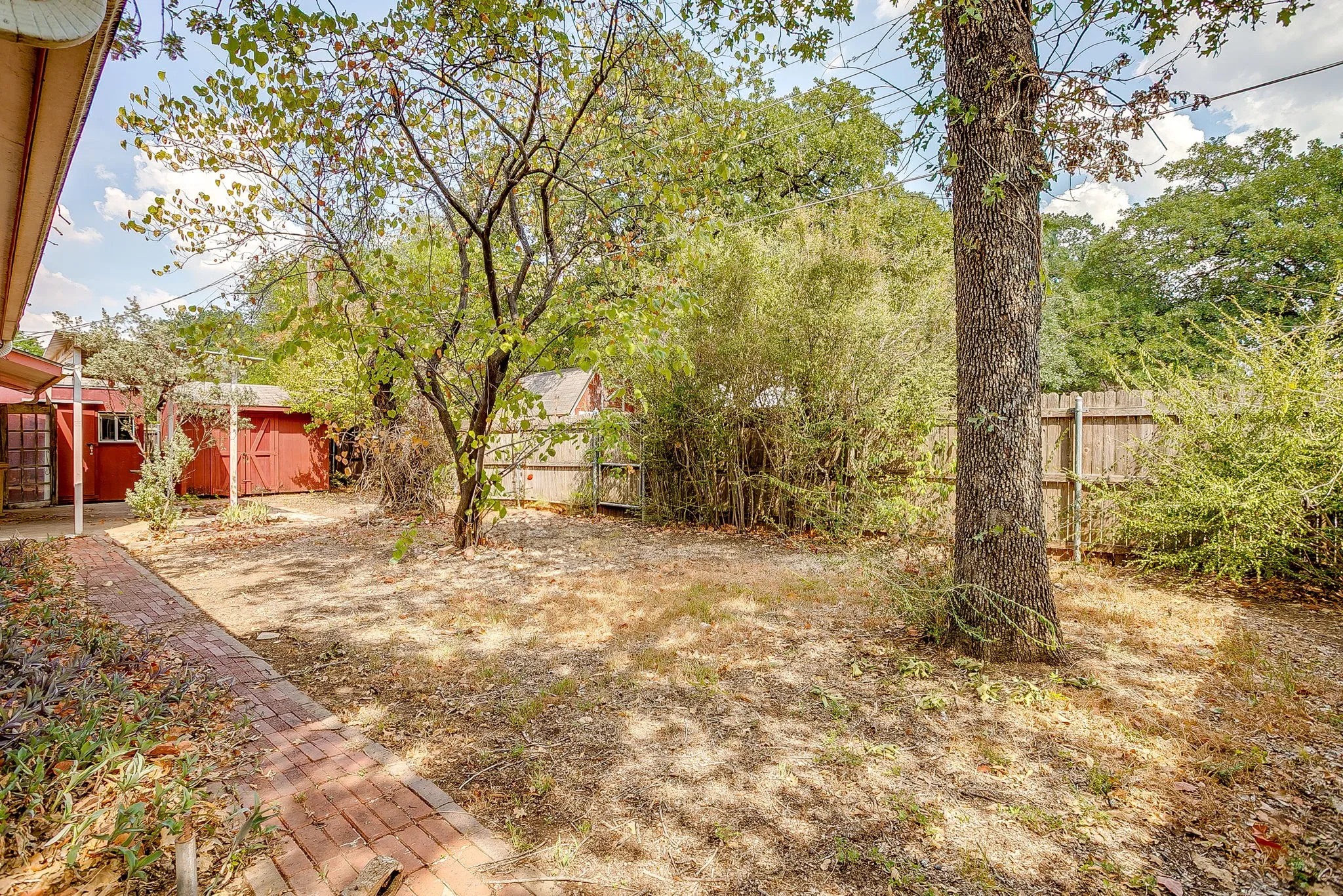 Rear yard featuring mature trees, wood fence, brick pathway, and a red shed