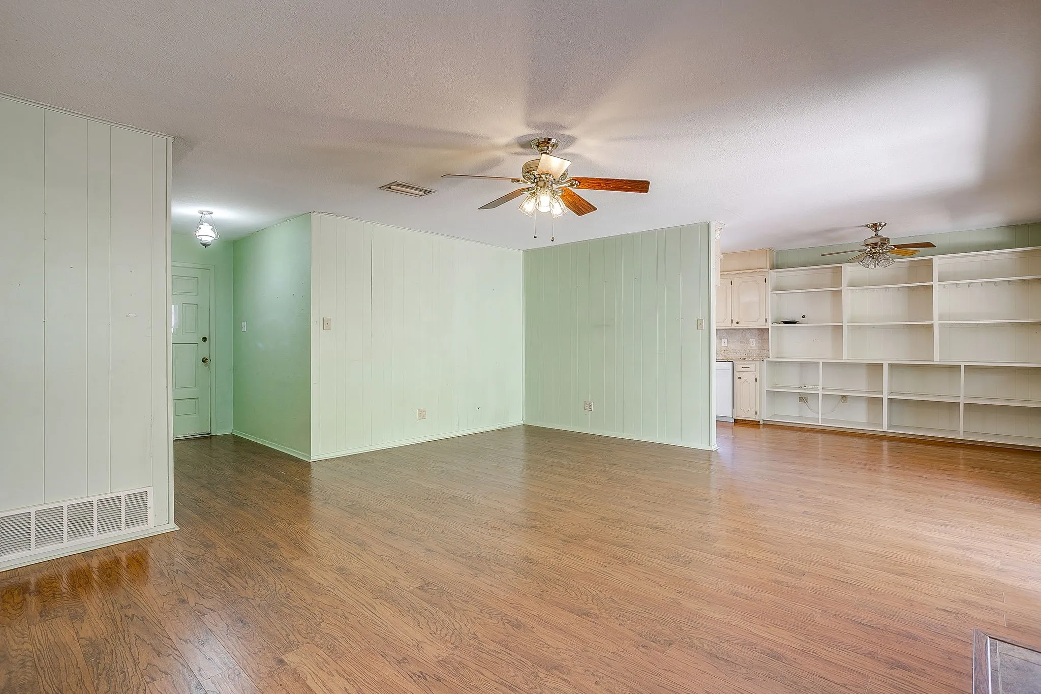 Wood-finish flooring throughout, featuring a built-in shelving unit, and multiple ceiling fans with integrated lighting