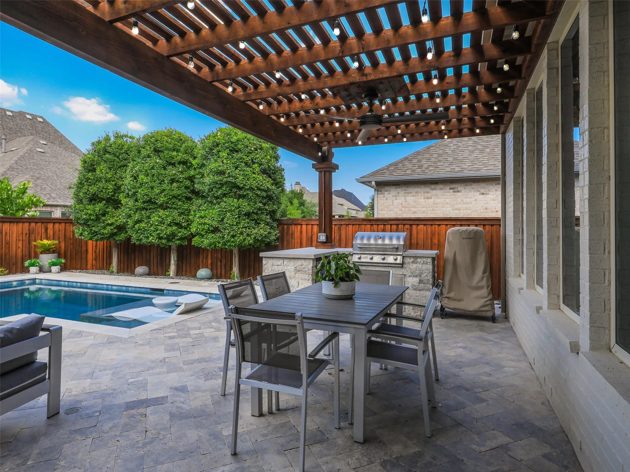 Beyond the pool, the fully fenced backyard features low-maintenance turf landscaping and a separate fire pit patio, creating multiple outdoor gathering spaces for entertaining, relaxing, and enjoying evenings at home. • Custom pool and spa ranging from 3.5 ft in the shallow end to 6 ft in the deep end, with basketball hoop
• Baja shelf with lounge chaises and table
• 5 Jandy pool lights, recently replaced
• Silver travertine decking throughout pool and patio
• Pergola over outdoor living area
• Built-in outdoor kitchen with Bull grill and Bull refrigerator
• Fire pit patio
• Artificial turf, approx. 21 ft x 38 ft
• Mature landscaping with landscape lighting
• Decorative rock: approx. 15 tons of large Texas black rock and 3 tons of black Mexican river stone
• Built-in speakers in the patio ceiling and throughout the pool and landscape areas