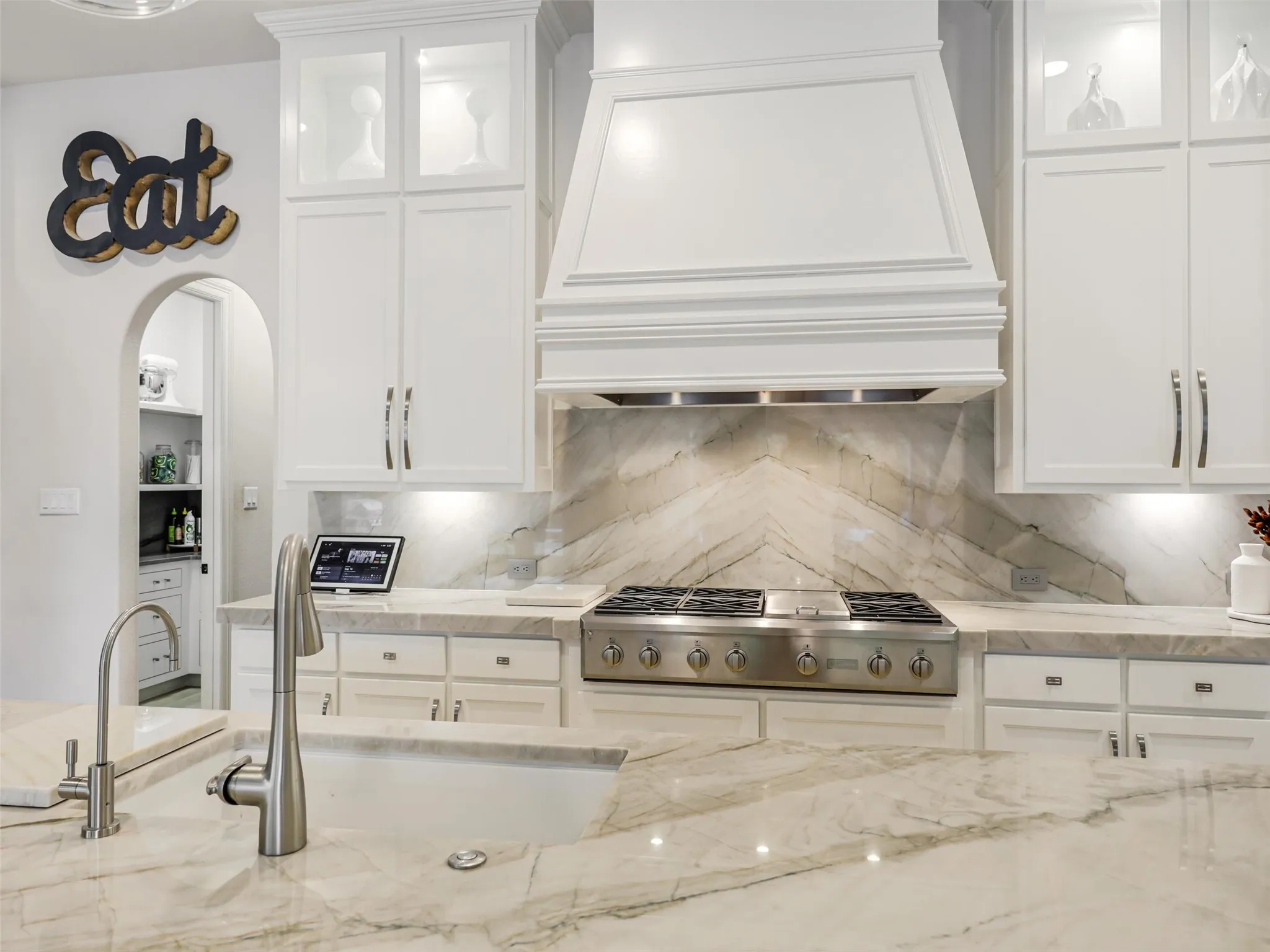 . Custom cabinetry provides abundant storage, while the oversized center island with breakfast bar offers additional prep and gathering space. Highend appliances include a built-in refrigerator, wine chiller, commercial-grade gas cooktop with vent hood, double ovens, and built-in microwave. • Quartzite waterfall countertops with matching quartzite backsplash
• Cabinets extended to the ceiling
• Custom pantry
• GE Monogram appliances: built-in refrigerator, double oven, and 48 inch range
• Built-in ice machine and wine refrigerator