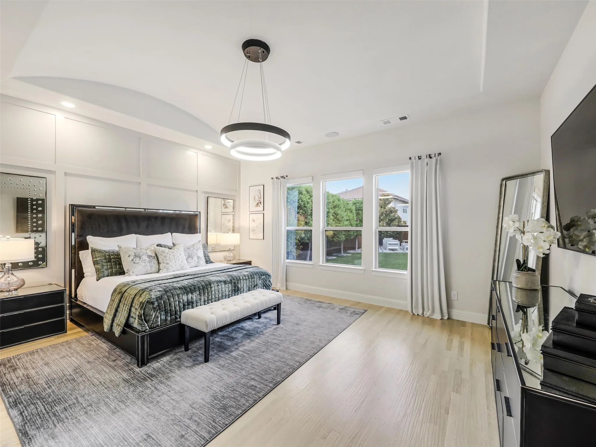 The downstairs primary retreat offers a private escape with a vaulted ceiling, chandelier, electric, remote-controlled shades, and a spacious ensuite bath. • White oak flooring
• Vaulted ceilings
• Custom accent wall