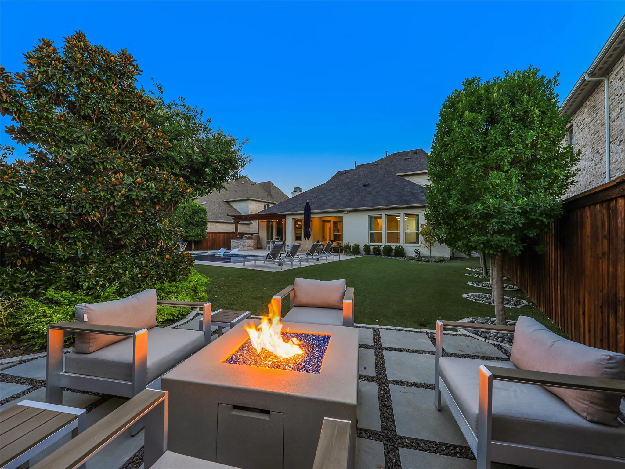 Beyond the pool, the fully fenced backyard features low-maintenance turf landscaping and a separate fire pit patio, creating multiple outdoor gathering spaces for entertaining, relaxing, and enjoying evenings at home. • Custom pool and spa ranging from 3.5 ft in the shallow end to 6 ft in the deep end, with basketball hoop
• Baja shelf with lounge chaises and table
• 5 Jandy pool lights, recently replaced
• Silver travertine decking throughout pool and patio
• Pergola over outdoor living area
• Built-in outdoor kitchen with Bull grill and Bull refrigerator
• Fire pit patio
• Artificial turf, approx. 21 ft x 38 ft
• Mature landscaping with landscape lighting
• Decorative rock: approx. 15 tons of large Texas black rock and 3 tons of black Mexican river stone
• Built-in speakers in the patio ceiling and throughout the pool and landscape areas