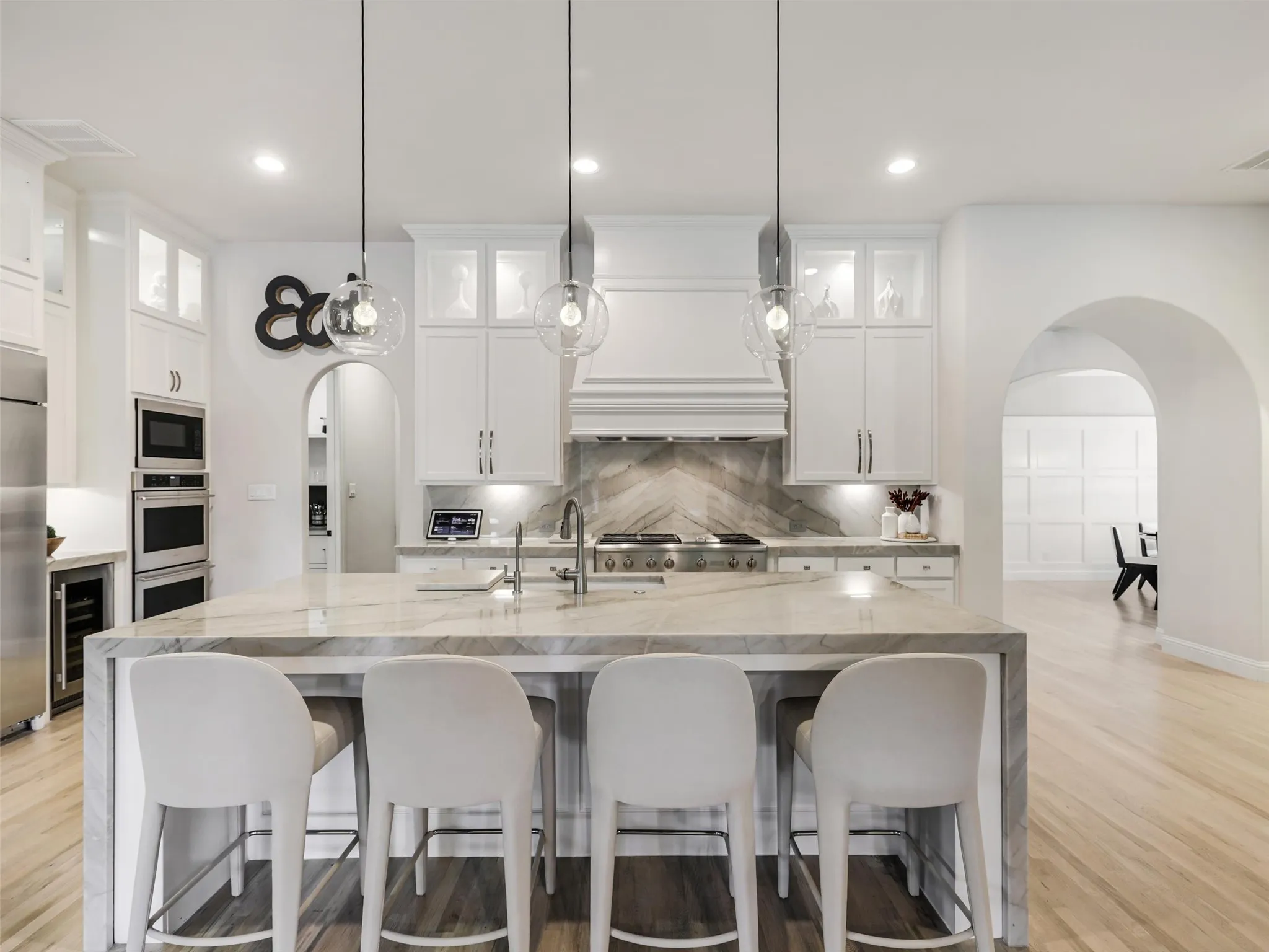. Custom cabinetry provides abundant storage, while the oversized center island with breakfast bar offers additional prep and gathering space. Highend appliances include a built-in refrigerator, wine chiller, commercial-grade gas cooktop with vent hood, double ovens, and built-in microwave. • Quartzite waterfall countertops with matching quartzite backsplash
• Cabinets extended to the ceiling
• Custom pantry
• GE Monogram appliances: built-in refrigerator, double oven, and 48 inch range
• Built-in ice machine and wine refrigerator