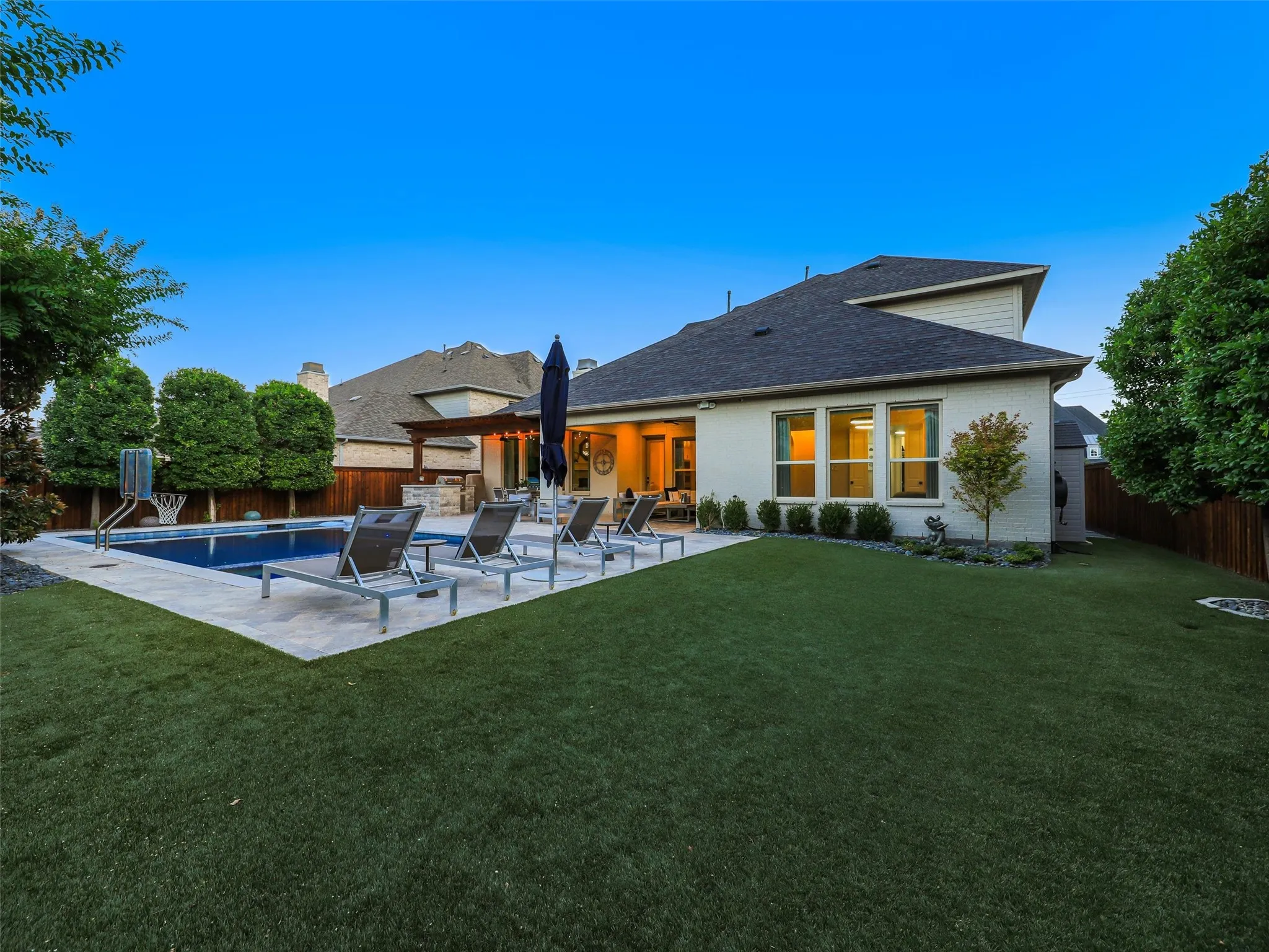 Beyond the pool, the fully fenced backyard features low-maintenance turf landscaping and a separate fire pit patio, creating multiple outdoor gathering spaces for entertaining, relaxing, and enjoying evenings at home. • Custom pool and spa ranging from 3.5 ft in the shallow end to 6 ft in the deep end, with basketball hoop
• Baja shelf with lounge chaises and table
• 5 Jandy pool lights, recently replaced
• Silver travertine decking throughout pool and patio
• Pergola over outdoor living area
• Built-in outdoor kitchen with Bull grill and Bull refrigerator
• Fire pit patio
• Artificial turf, approx. 21 ft x 38 ft
• Mature landscaping with landscape lighting
• Decorative rock: approx. 15 tons of large Texas black rock and 3 tons of black Mexican river stone
• Built-in speakers in the patio ceiling and throughout the pool and landscape areas