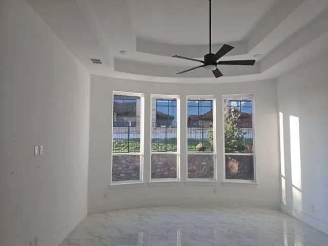 Spacious room featuring a tray ceiling with a ceiling fan, white walls, and large windows with black security bars