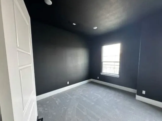 Recessed ceiling lighting, dark wall finish, white trim, window with security bars, and light-colored carpeting