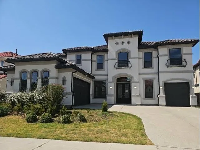 Stucco exterior with a tile roof, arched windows, decorative iron balconies, and an integrated two-car garage