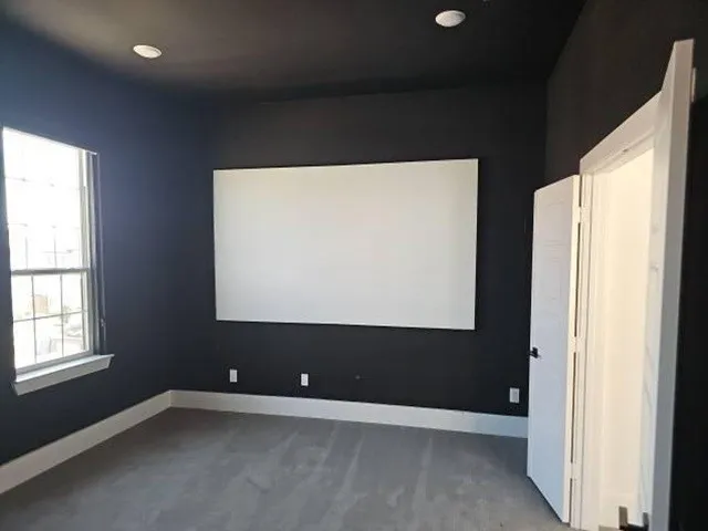 Recessed ceiling lighting, dark wall finish, window with white trim, wall-mounted screen, and carpeted flooring