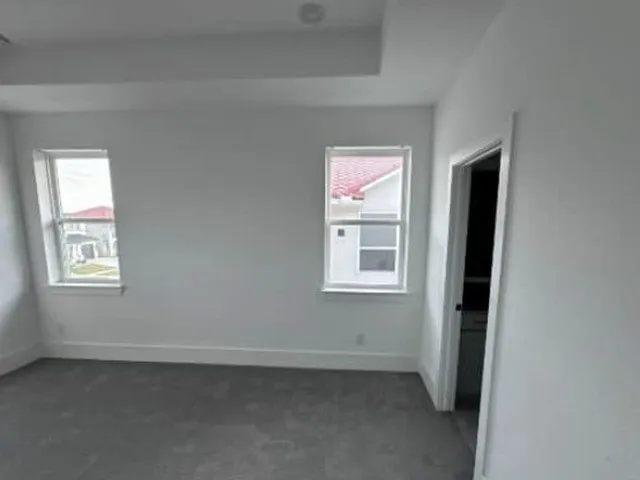 Recessed lighting, tray ceiling, two windows, wall-to-wall carpeting, and a white interior door with a dark handle
