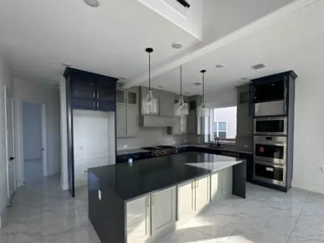 Gourmet kitchen with an expansive island, light gray and navy cabinetry, stainless steel built-in appliances, and pendant lighting