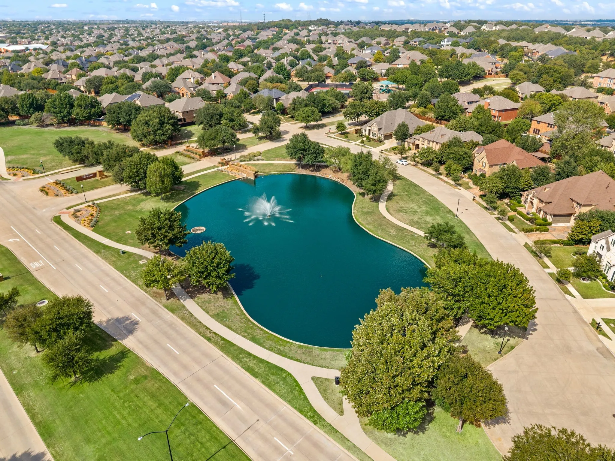 Central community pond with a fountain, surrounded by paved walking paths and mature trees