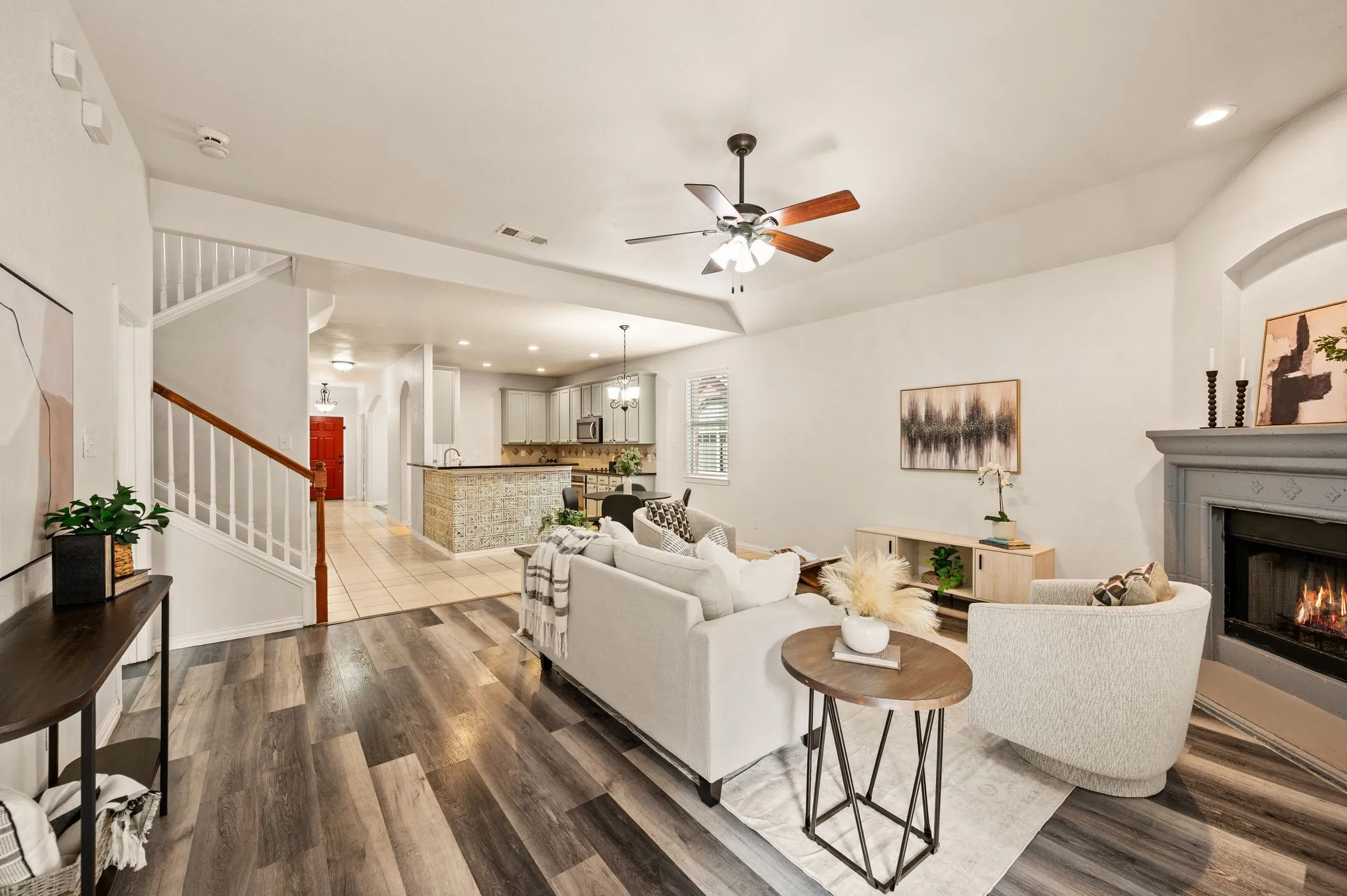 Vaulted ceiling with a ceiling fan, wood-finish flooring, fireplace with a decorative mantel, and a staircase with wood handrails