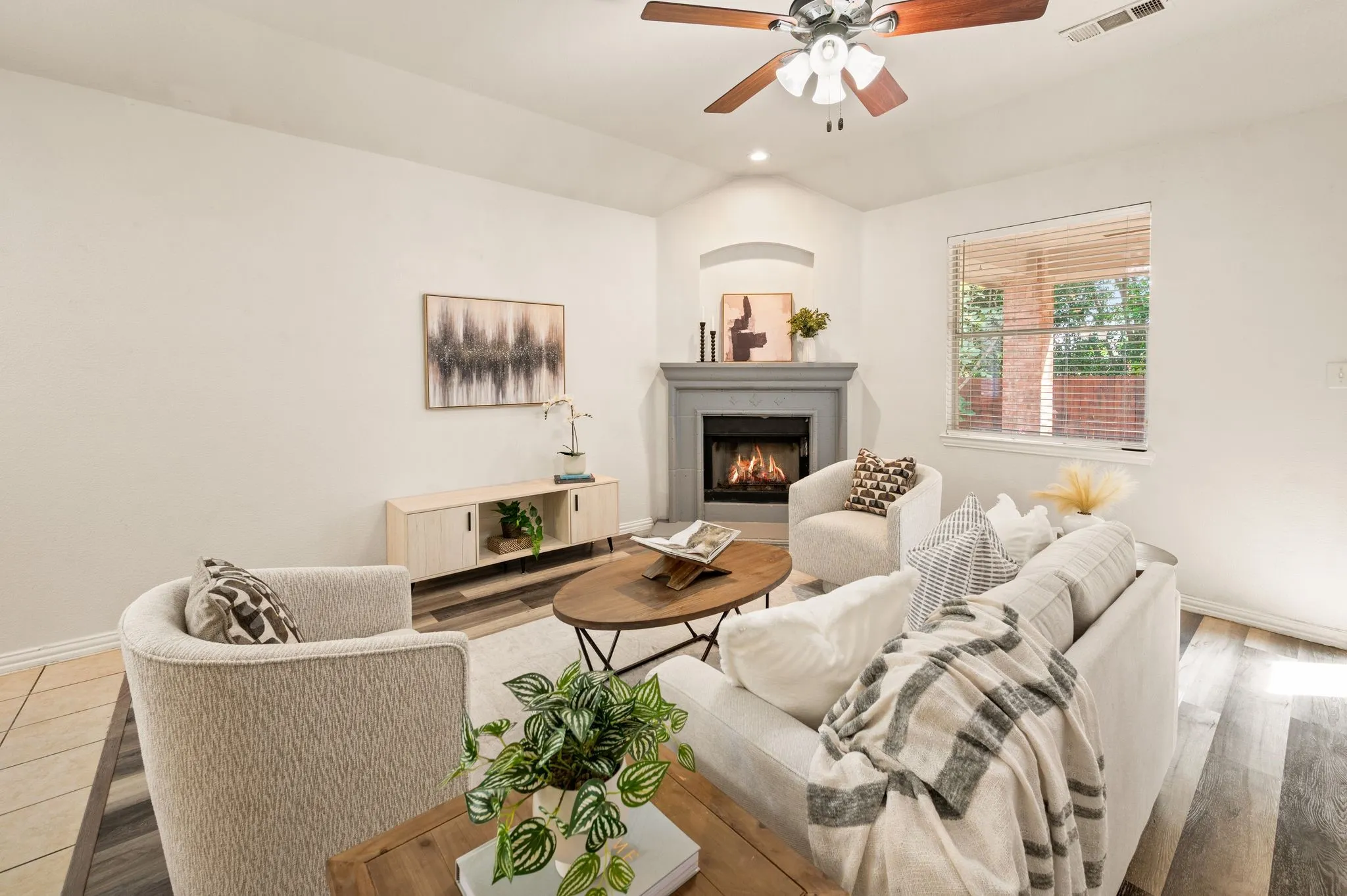 Living space featuring a corner fireplace, vaulted ceiling, ceiling fan, and wood-finish flooring