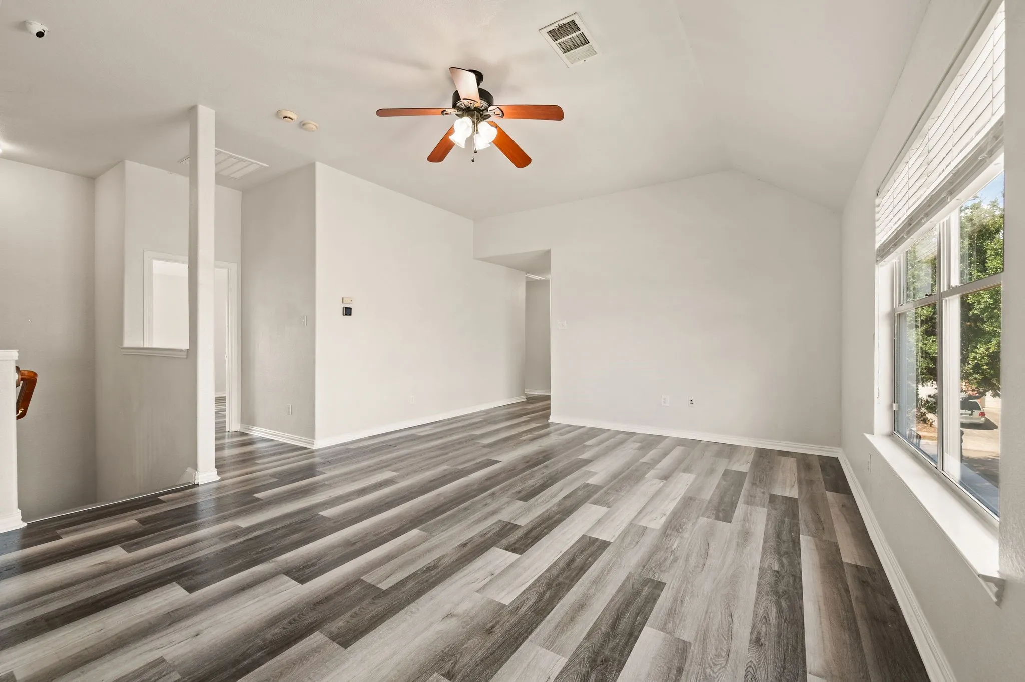 Vaulted ceiling with an attached ceiling fan and light fixture, wood-finish flooring, and a window with blinds