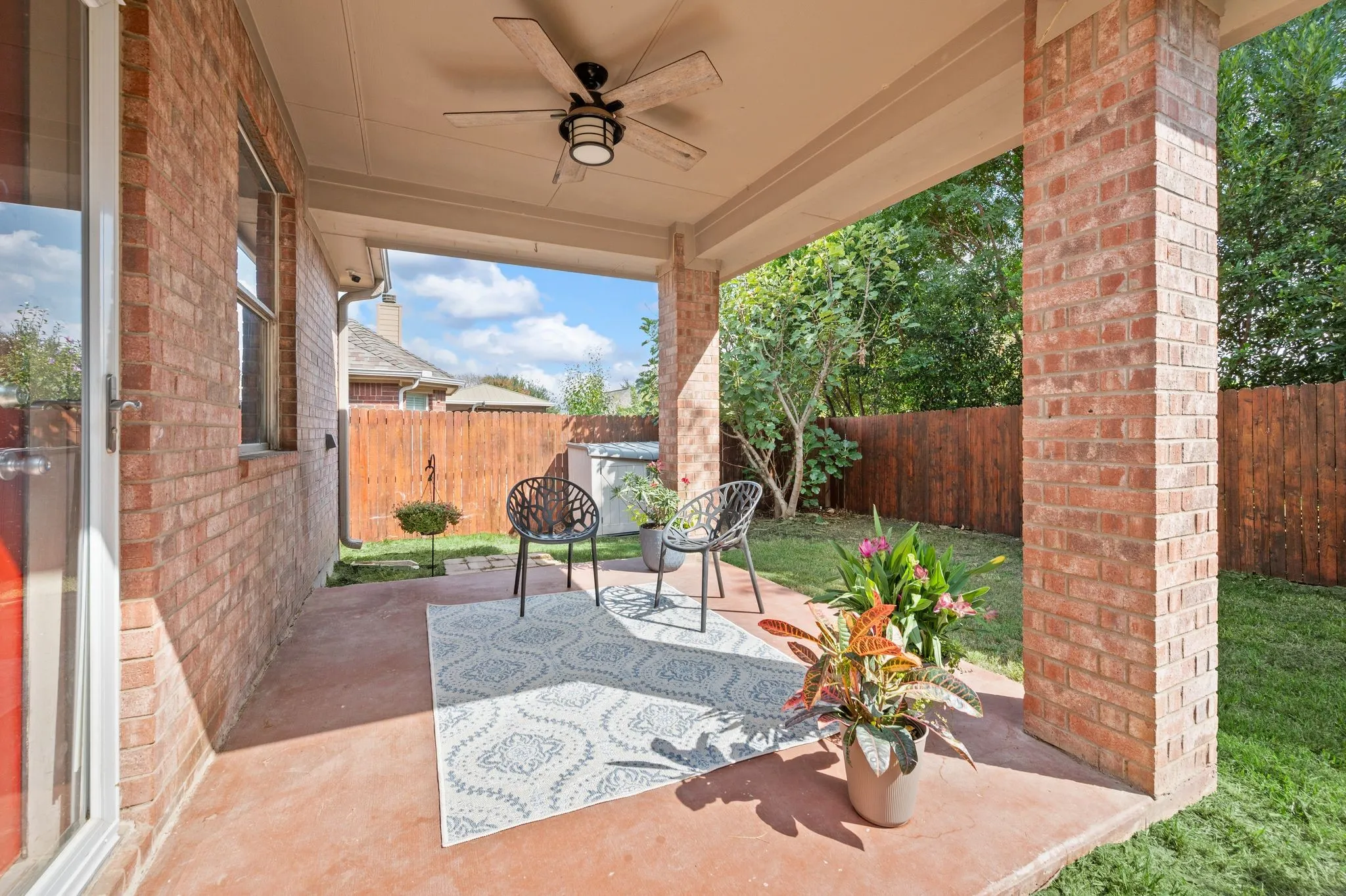 Covered patio featuring a ceiling fan, brick columns, and a stained concrete surface