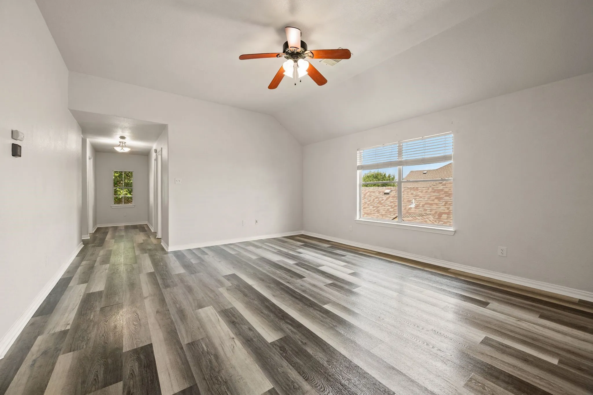 Vaulted ceiling with a ceiling fan, multiple windows, wood-finish flooring, and recessed lighting in the hallway