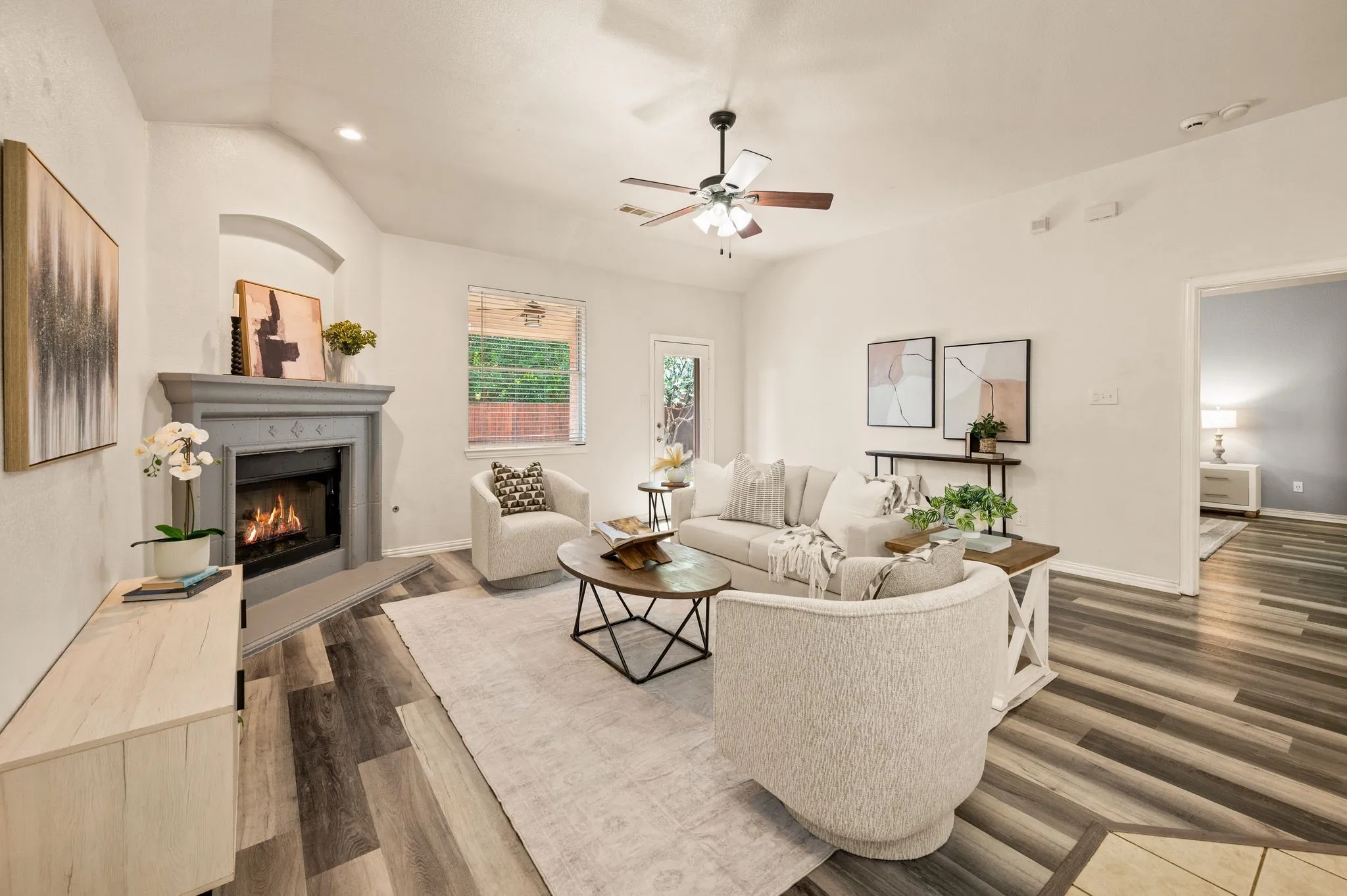 Vaulted ceiling with a ceiling fan, fireplace with a mantel, wood-finish flooring, and natural light from a window