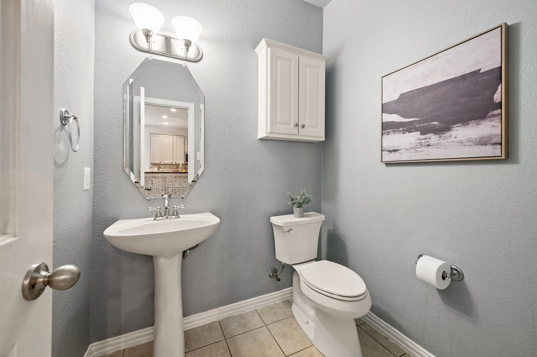Pedestal sink with chrome faucet, octagonal wall mirror, and overhead vanity lighting