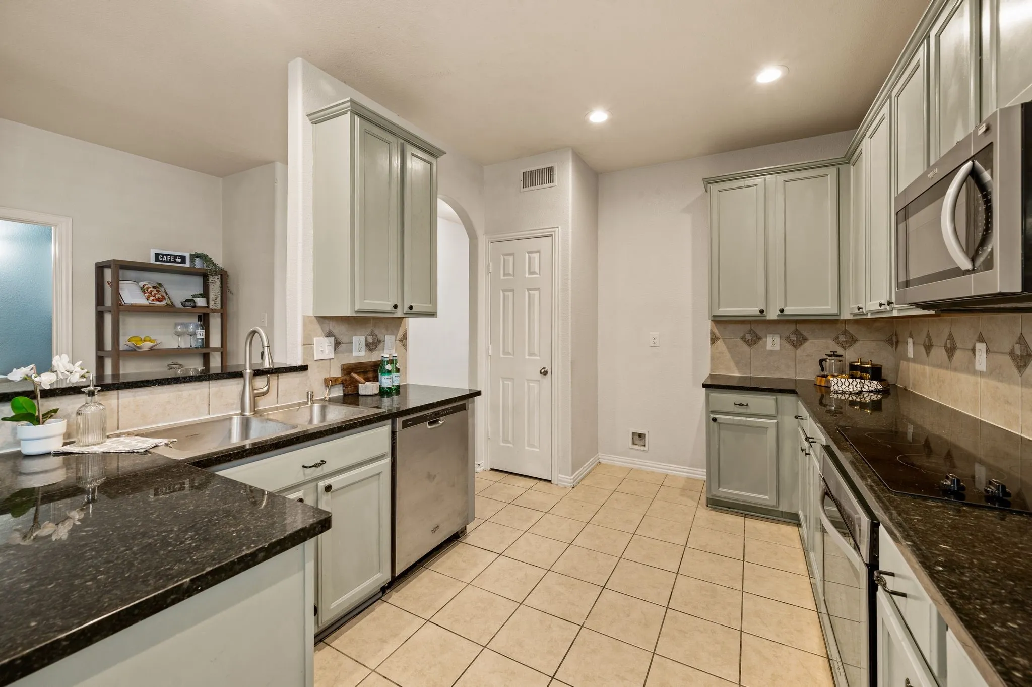 Kitchen featuring light-toned cabinetry, dark countertops, a tile backsplash, stainless steel appliances, and recessed lighting