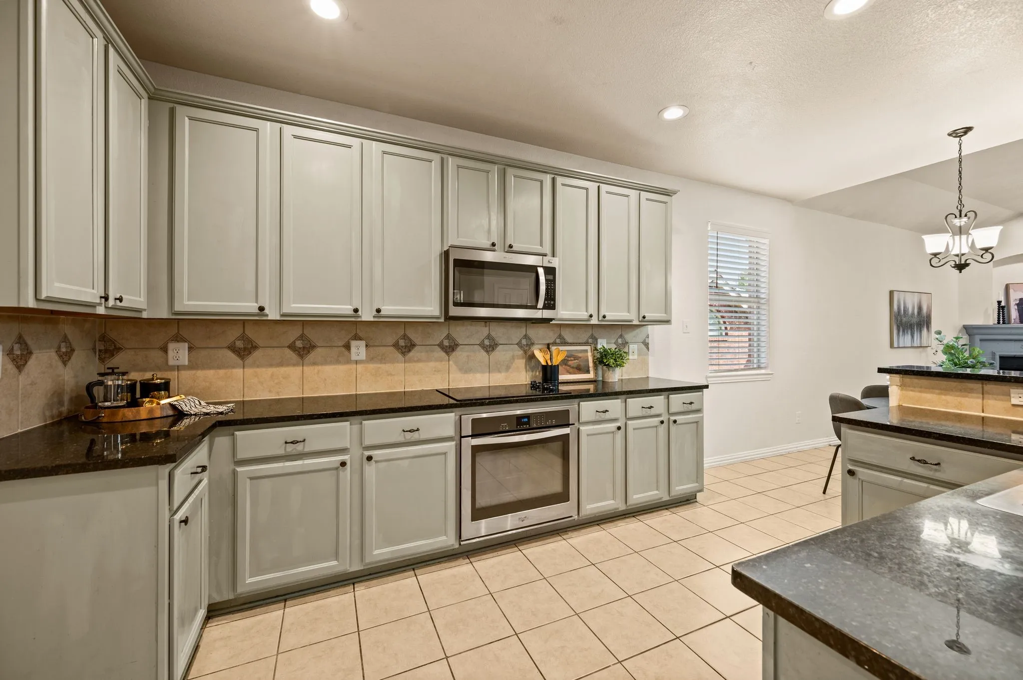 Kitchen featuring light-toned cabinetry, dark countertops, a tile backsplash, stainless steel appliances, and tiled flooring