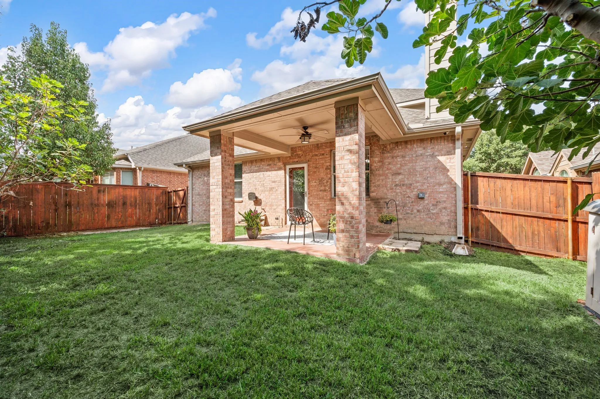 Expansive green lawn with a covered patio featuring a ceiling fan and brick columns
