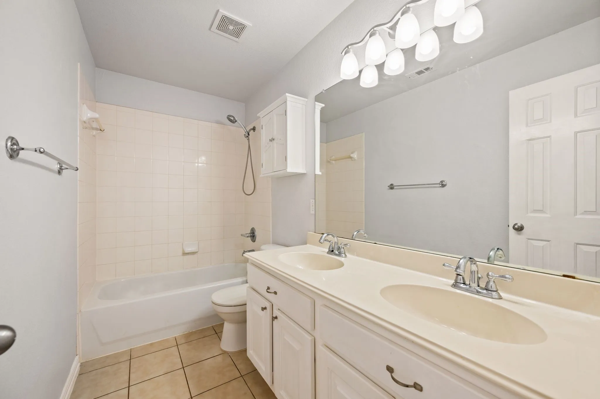 Double vanity with integrated sinks, white cabinetry, chrome fixtures, and a large wall-mounted mirror