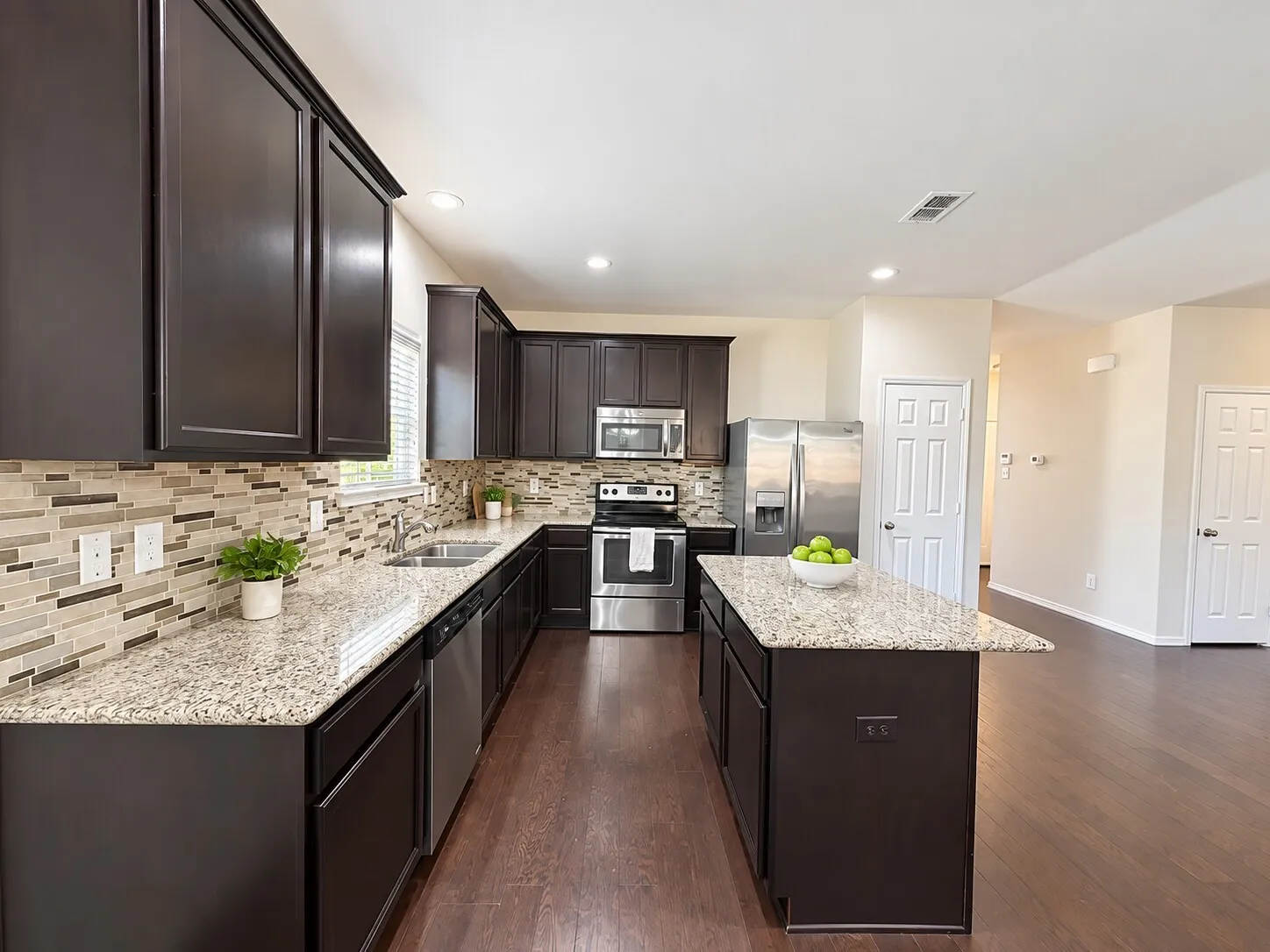 Kitchen featuring dark wood-finish cabinetry, light-toned countertops, stainless steel appliances, a mosaic tile backsplash, and wood-finish flooring
